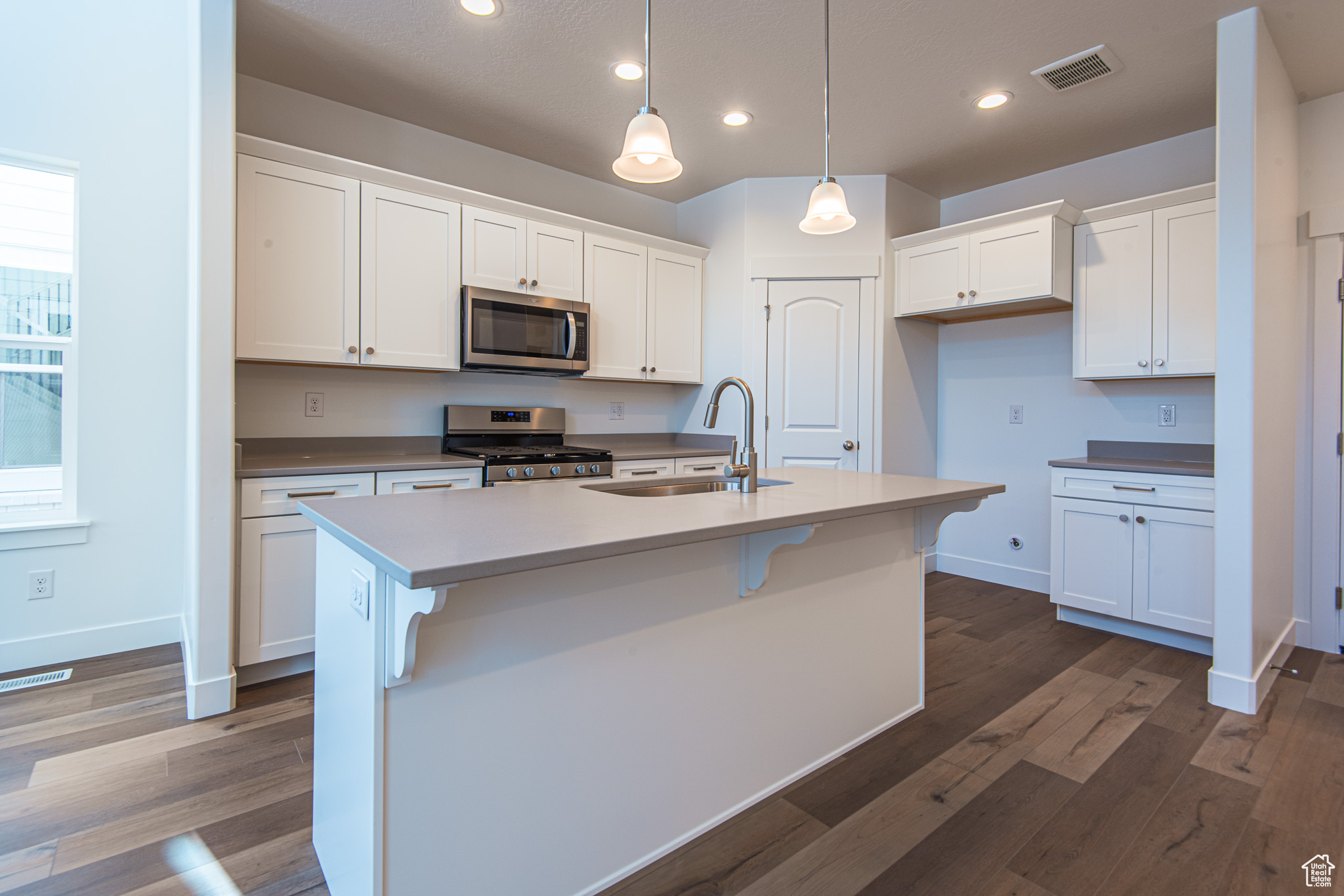 Kitchen with dark hardwood / wood-style flooring, appliances with stainless steel finishes, an island with sink, white cabinets, and sink