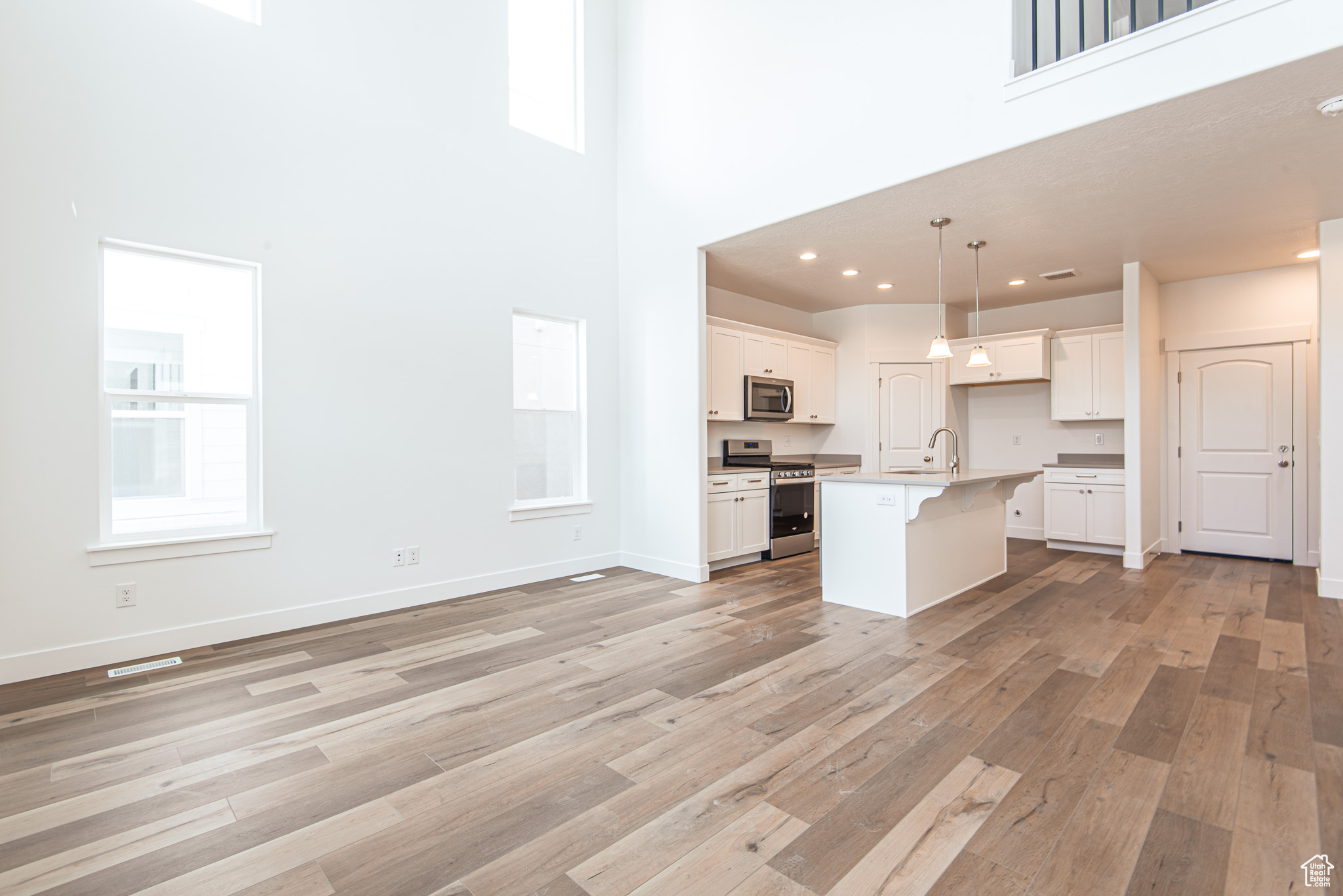 Kitchen with a high ceiling, a center island with sink, light hardwood / wood-style floors, and appliances with stainless steel finishes