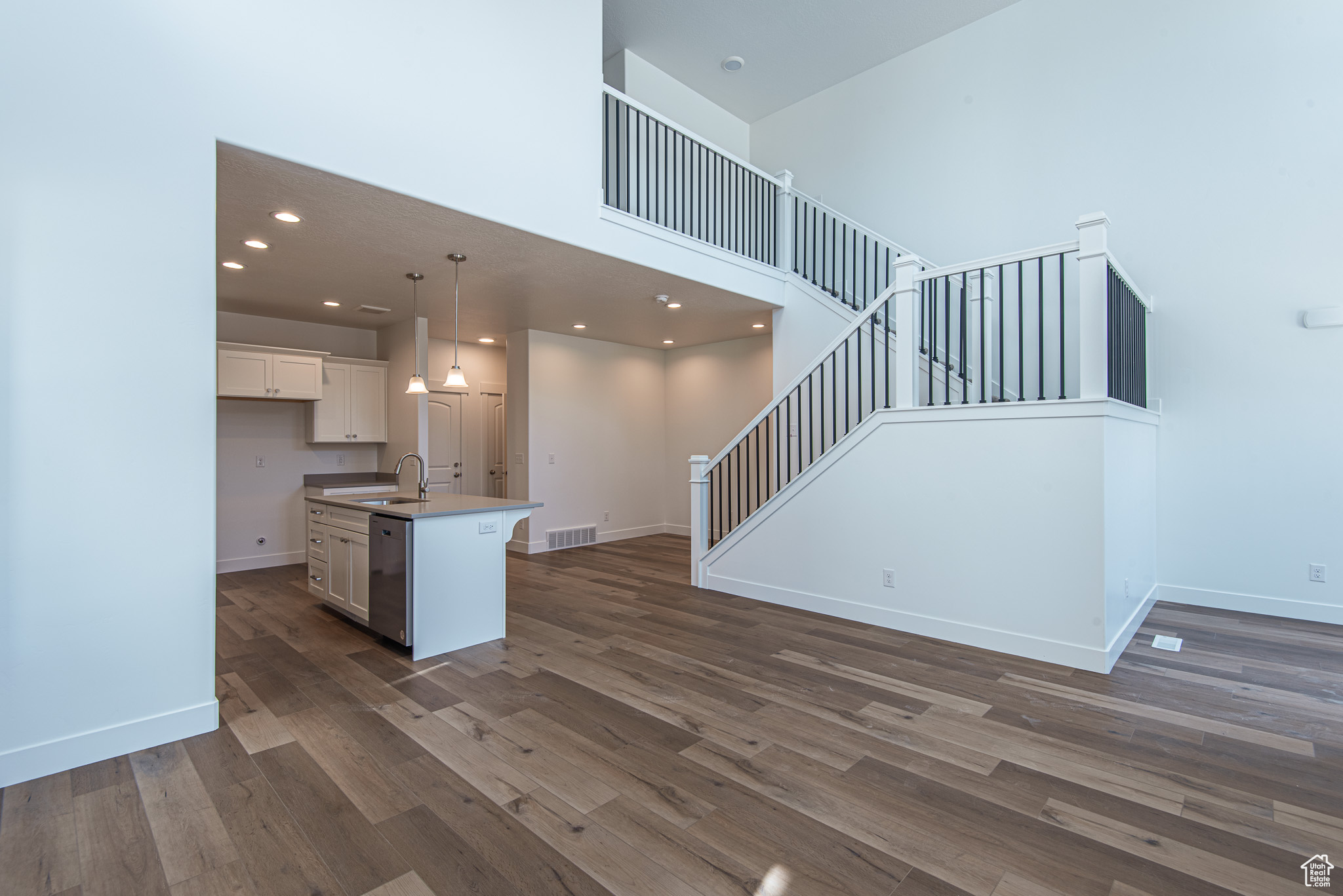 Kitchen featuring a center island with sink, white cabinets, dark hardwood / wood-style floors, decorative light fixtures, and a high ceiling