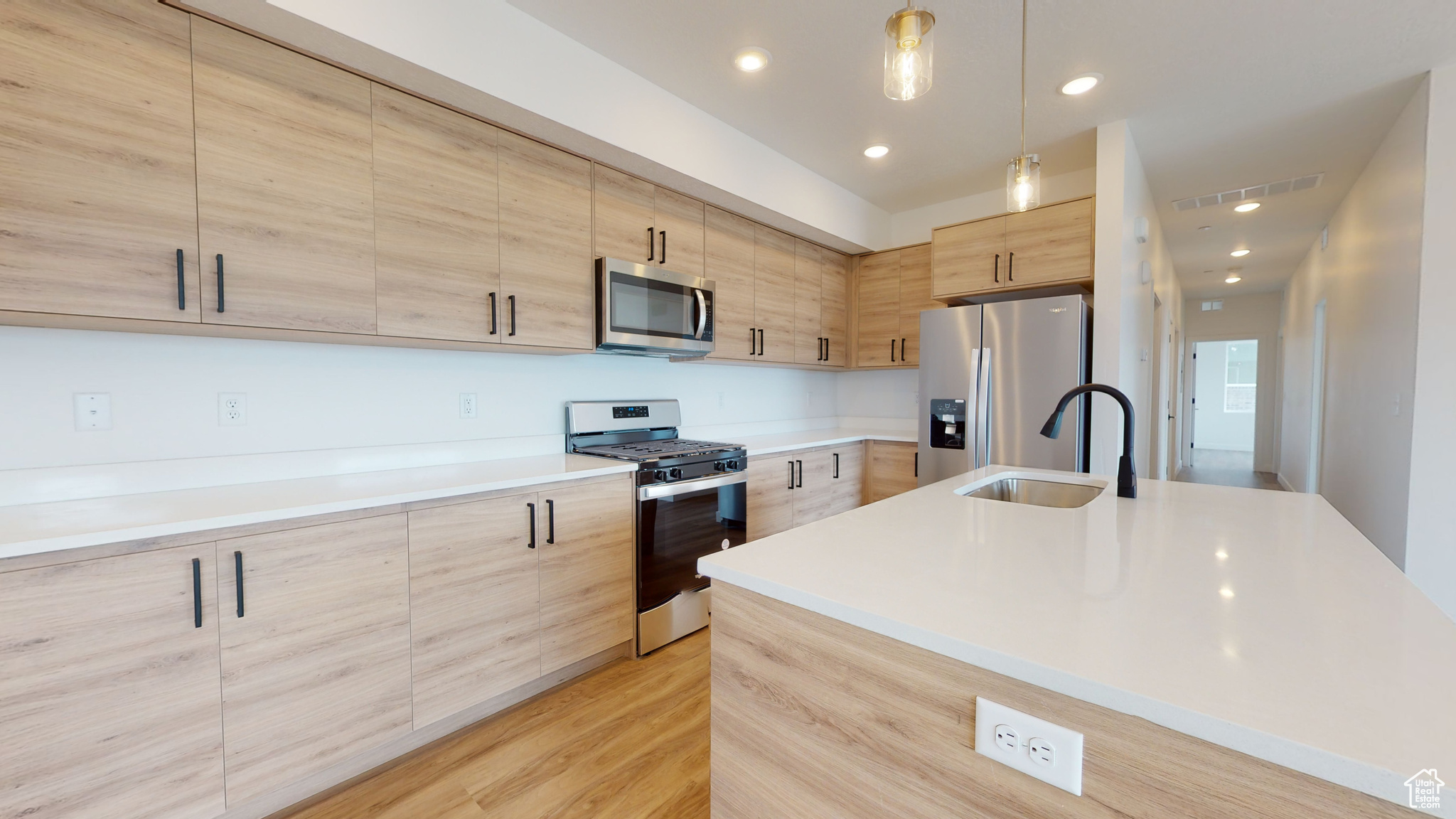 Kitchen with decorative light fixtures, appliances with stainless steel finishes, light hardwood / wood-style flooring, an island with sink, and sink