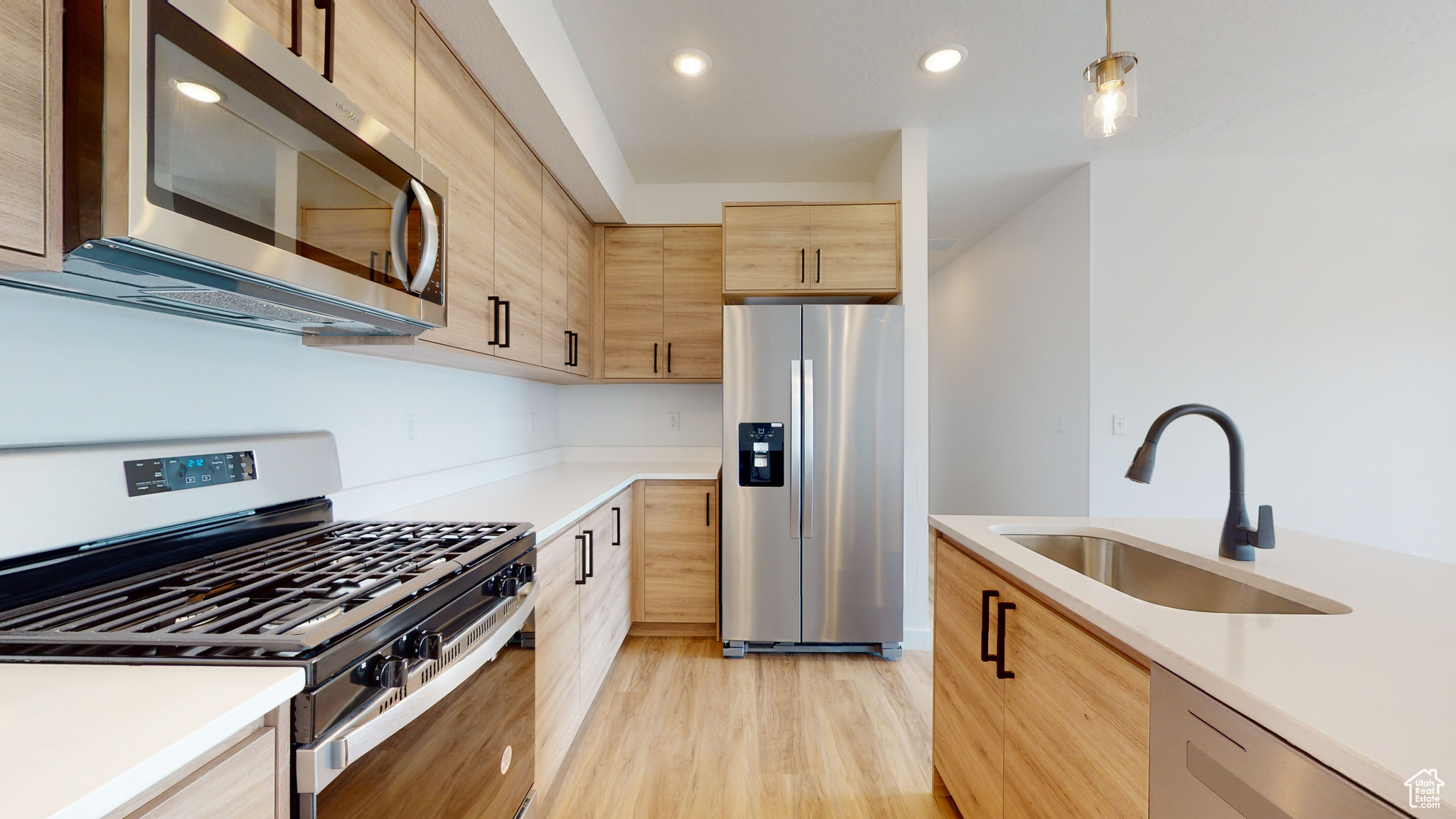 Kitchen featuring light brown cabinets, appliances with stainless steel finishes, decorative light fixtures, light hardwood / wood-style flooring, and sink