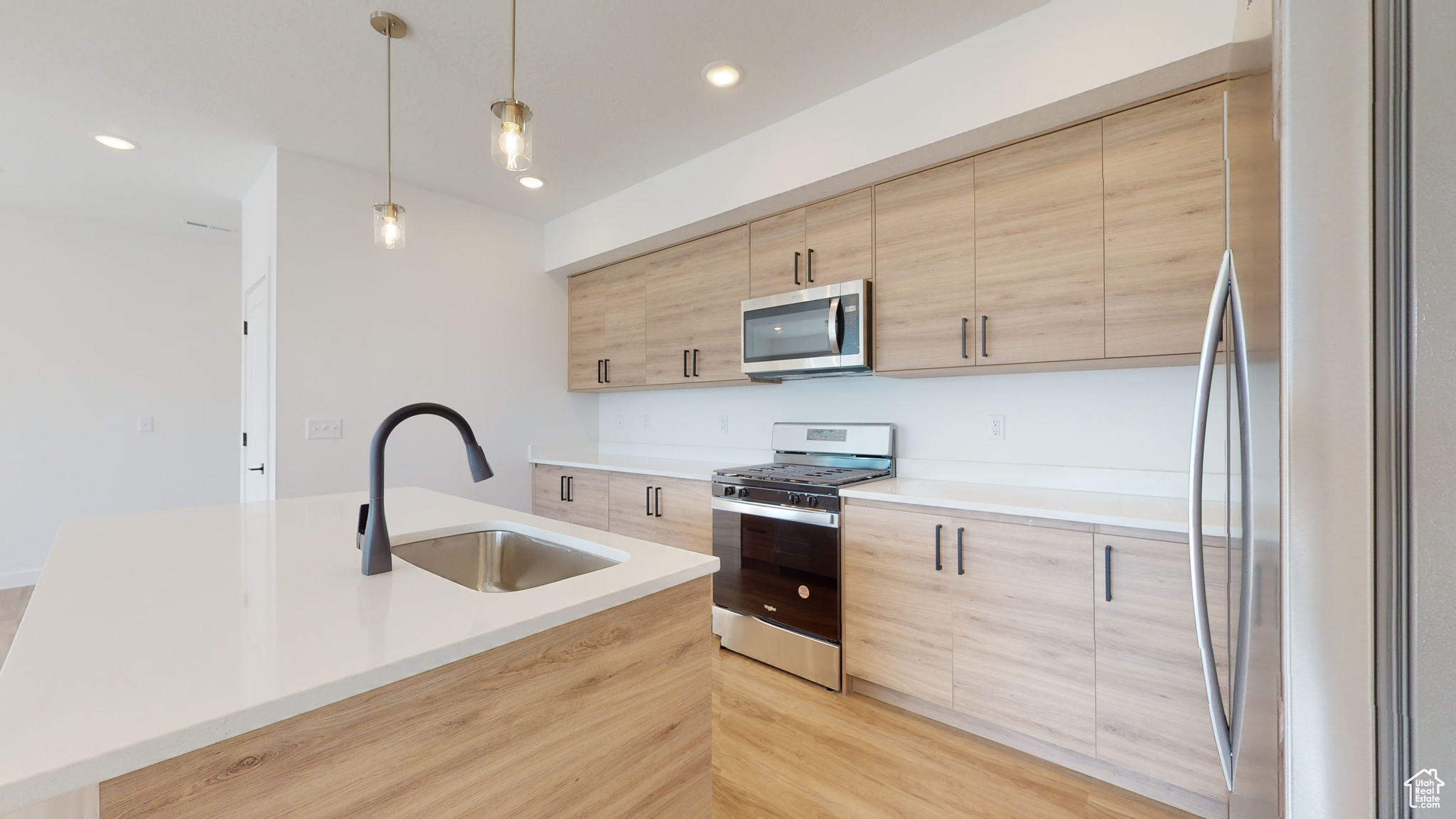Kitchen featuring light brown cabinets, a kitchen island with sink, appliances with stainless steel finishes, decorative light fixtures, and sink
