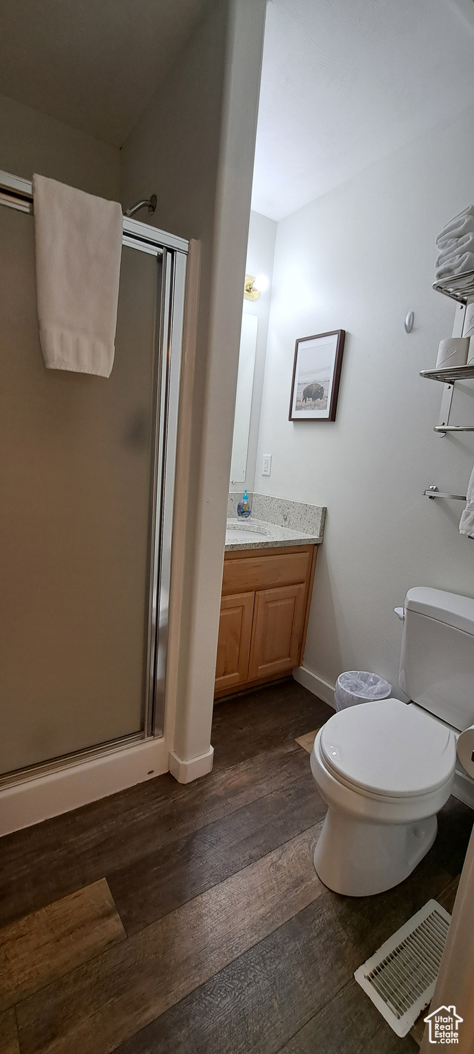 Bathroom with an enclosed shower, vanity, toilet, and hardwood / wood-style flooring