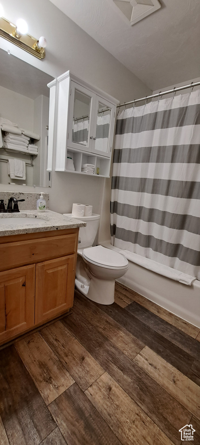 Full bathroom with toilet, hardwood / wood-style floors, shower / bathtub combination with curtain, and oversized vanity