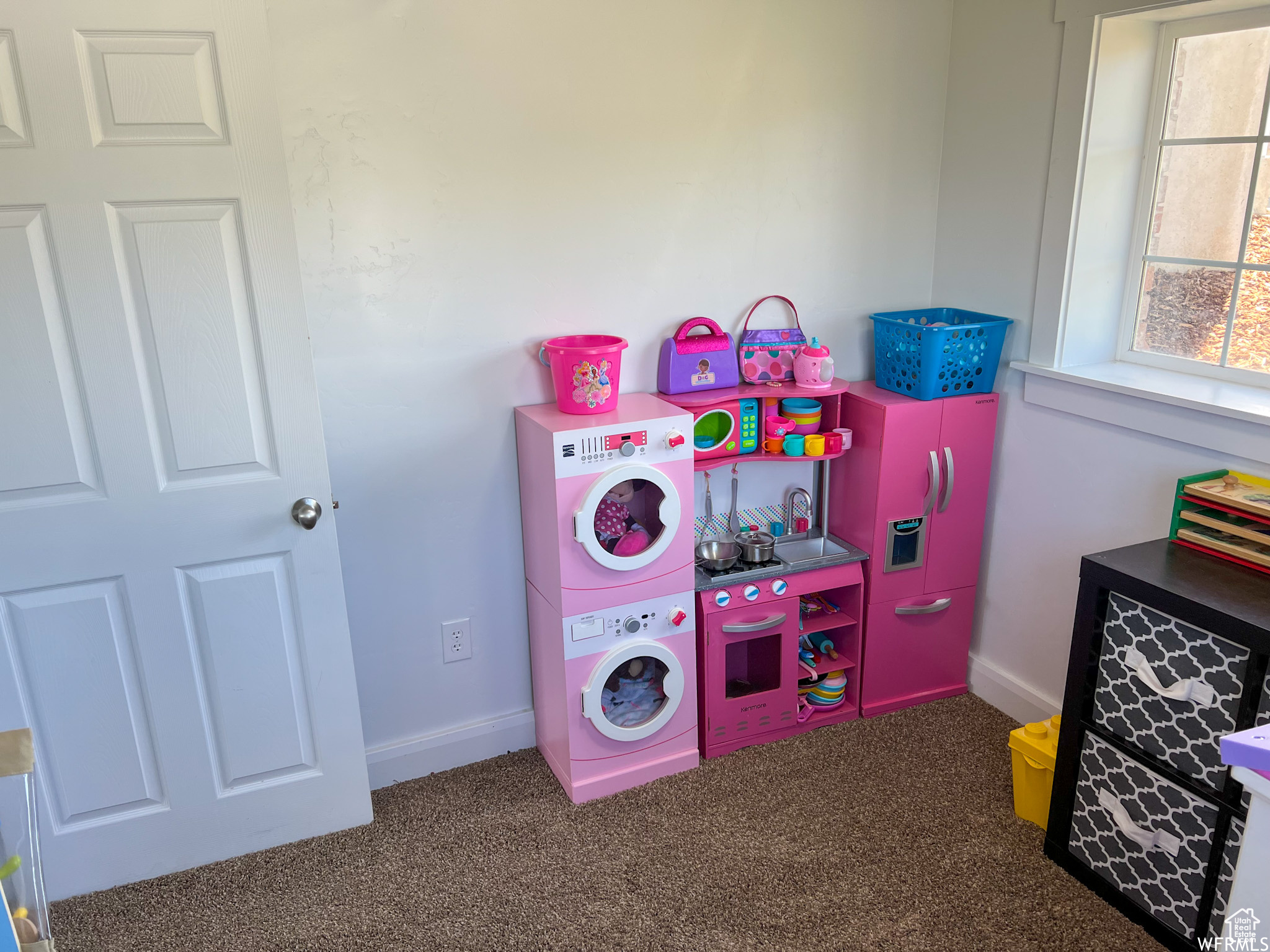 Playroom with stacked washing maching and dryer and dark colored carpet