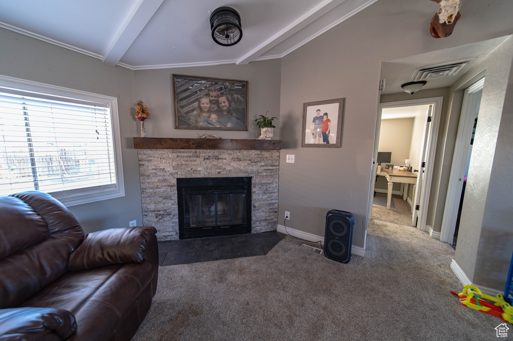 Living room featuring a stone fireplace, vaulted ceiling with beams, and dark carpet