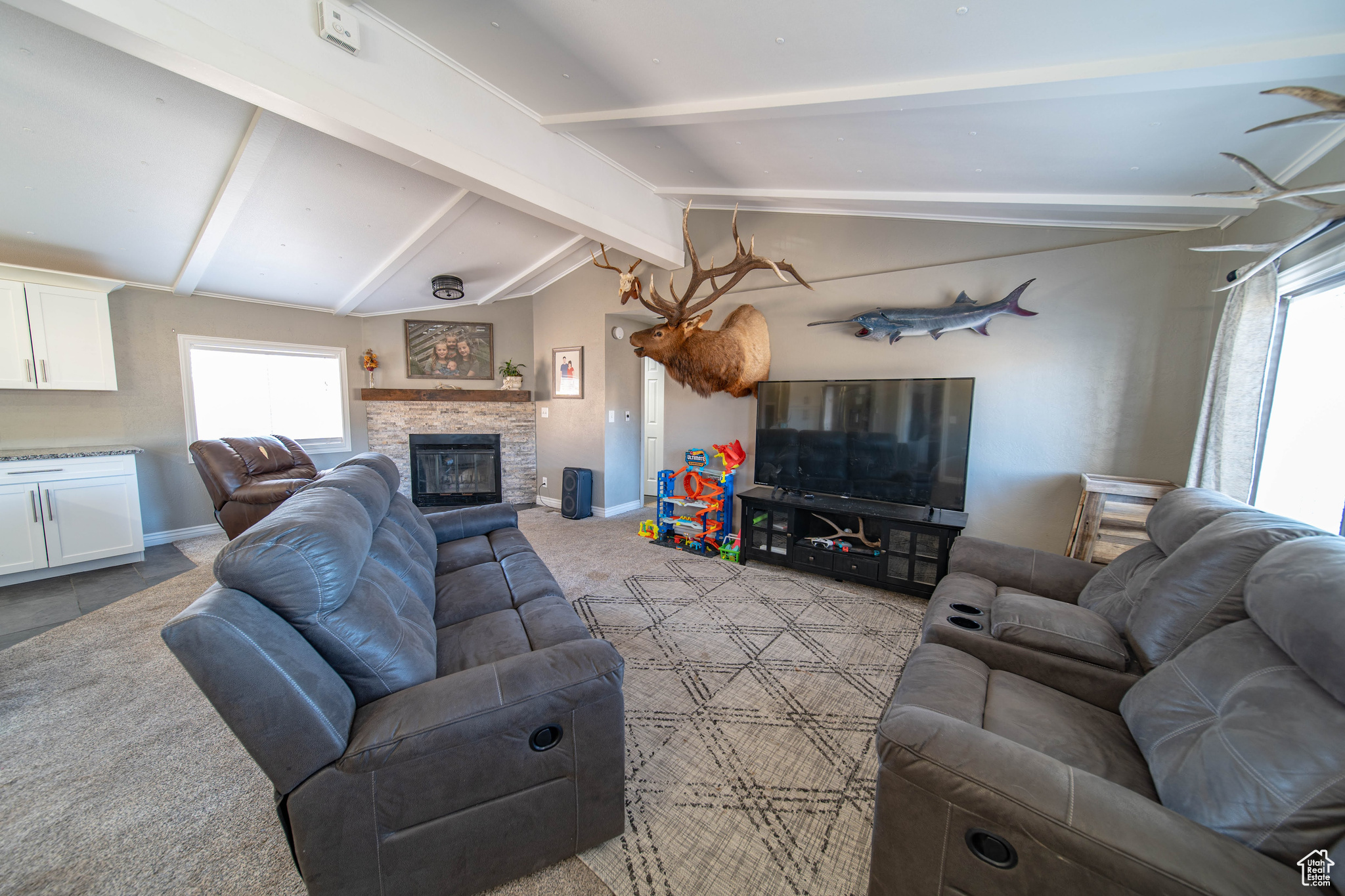 Tiled living room featuring a stone fireplace, vaulted ceiling with beams, and a healthy amount of sunlight