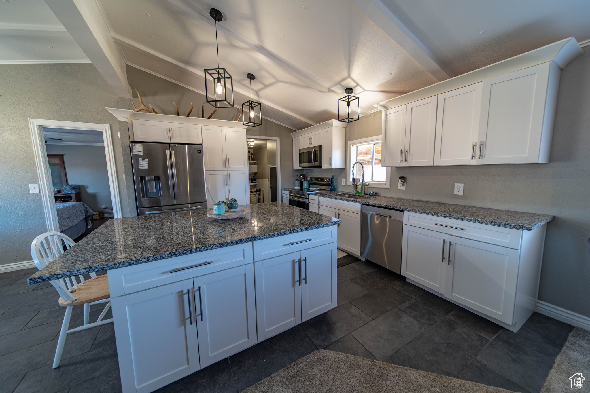 Kitchen with dark stone countertops, white cabinetry, hanging light fixtures, and stainless steel appliances