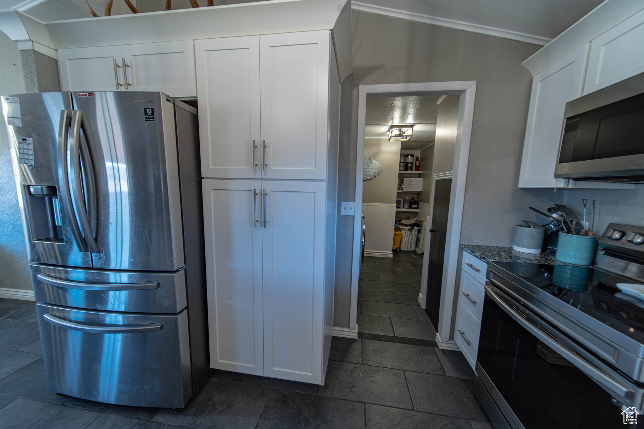 Kitchen featuring crown molding, dark tile flooring, appliances with stainless steel finishes, white cabinets, and dark stone countertops