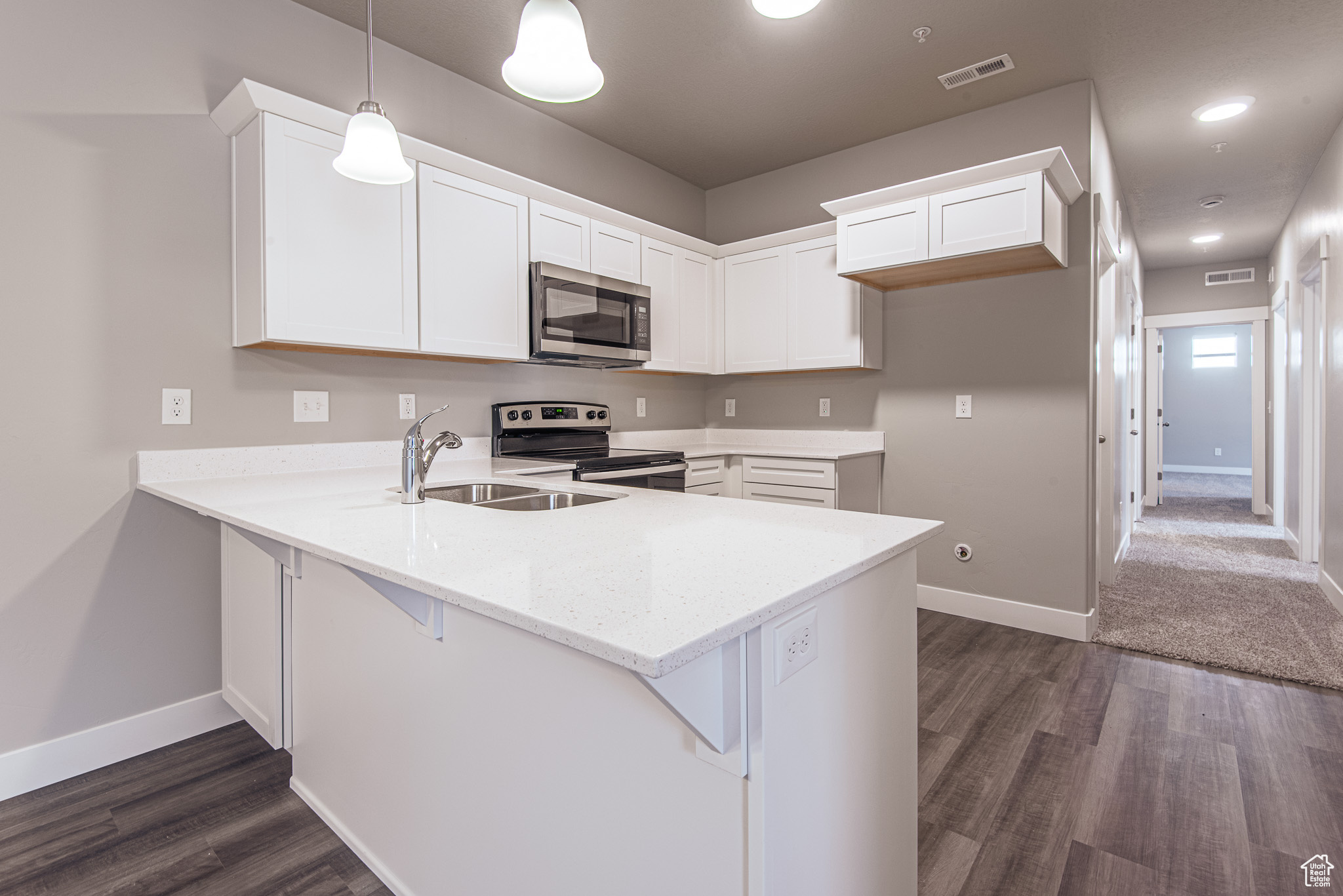 Kitchen featuring dark hardwood / wood-style flooring, stainless steel appliances, white cabinets, kitchen peninsula, and decorative light fixtures