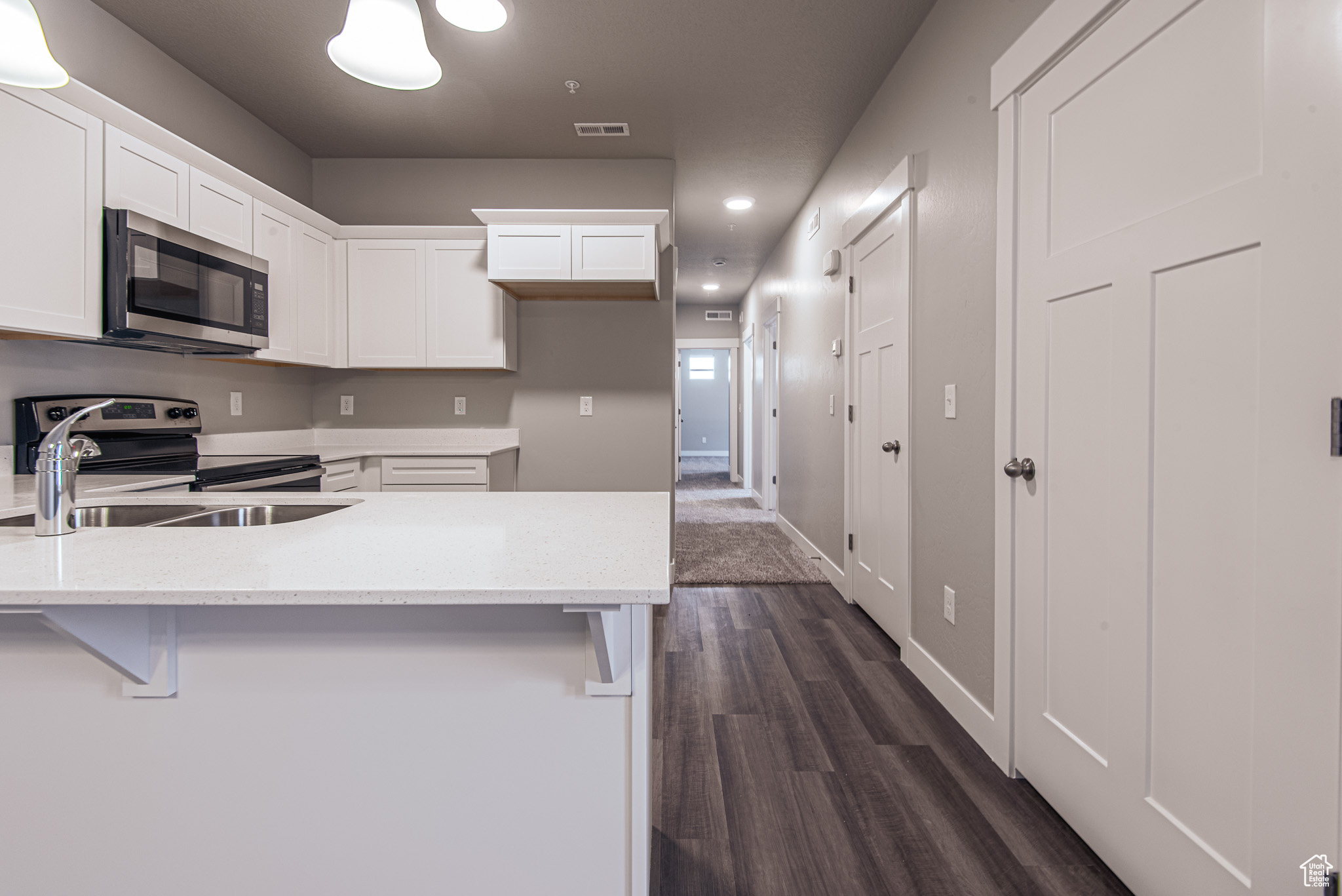 Kitchen featuring dark hardwood / wood-style floors, light stone countertops, stainless steel appliances, a breakfast bar, and white cabinetry