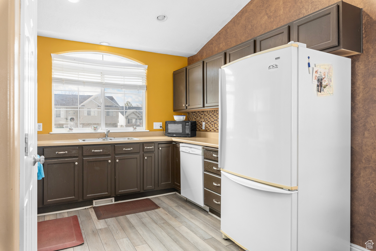 Kitchen featuring light hardwood / wood-style floors, white appliances, sink, vaulted ceiling, and tasteful backsplash