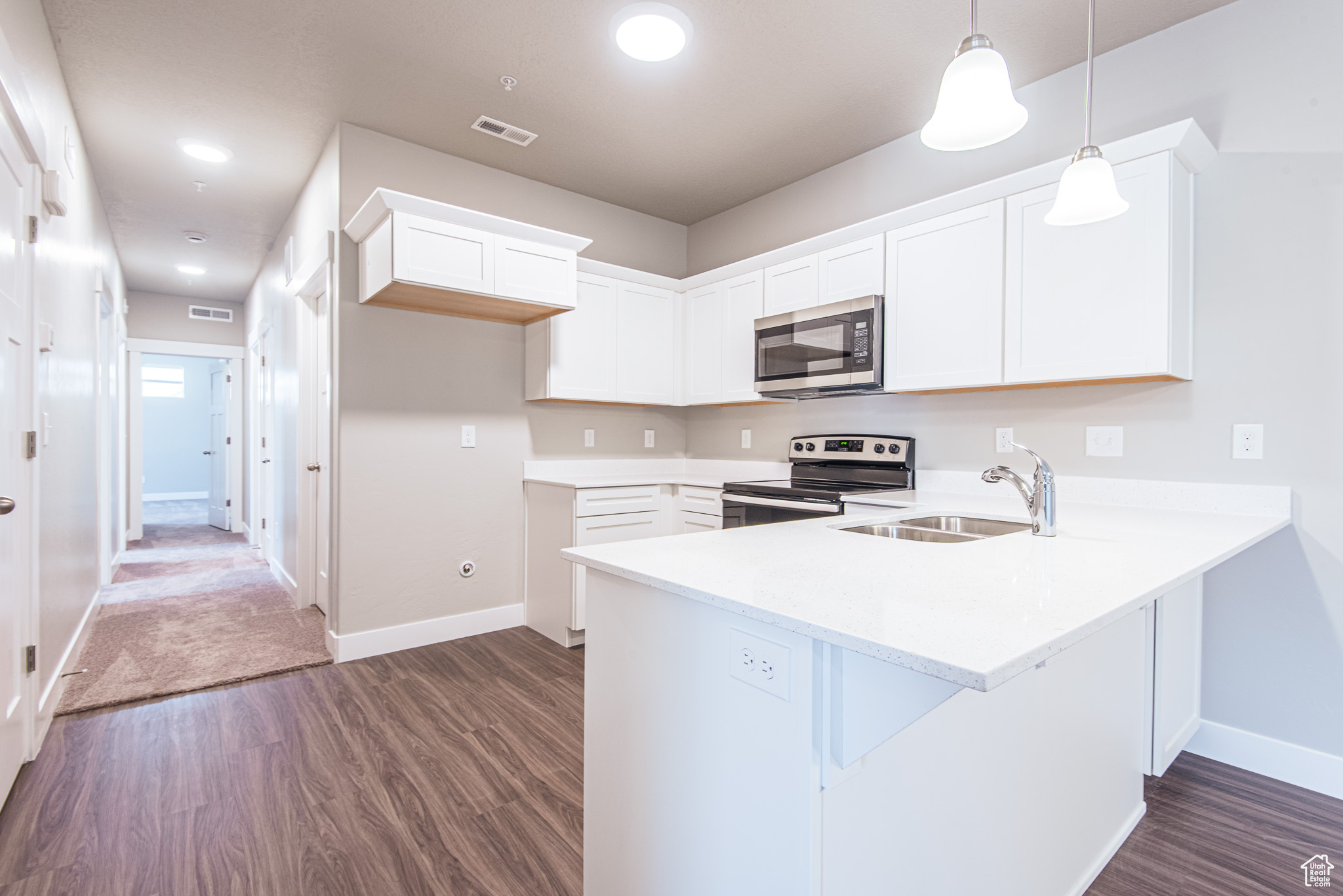 Kitchen featuring dark hardwood / wood-style floors, kitchen peninsula, sink, white cabinets, and appliances with stainless steel finishes