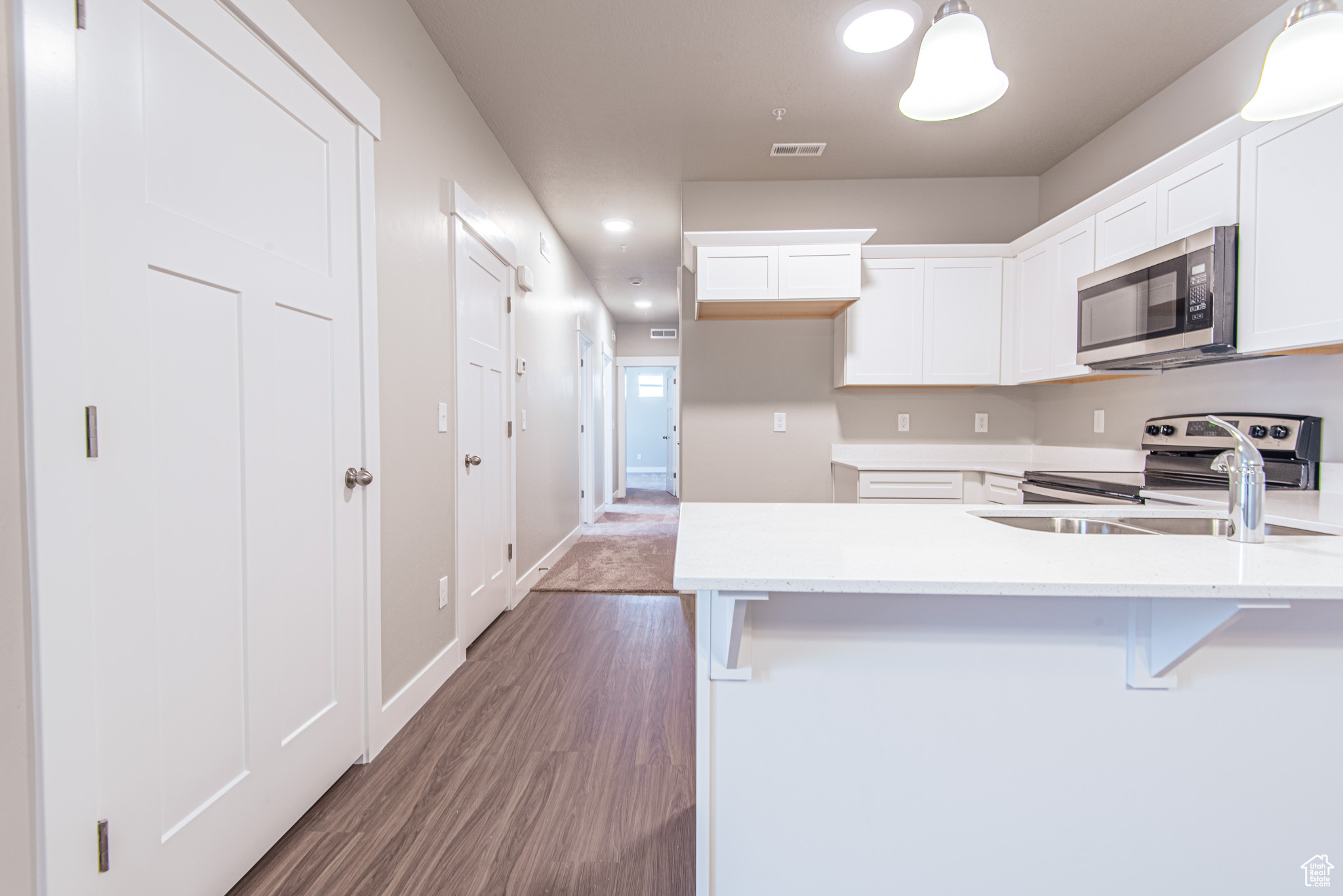 Kitchen with white cabinetry, hanging light fixtures, dark hardwood / wood-style floors, electric range, and sink