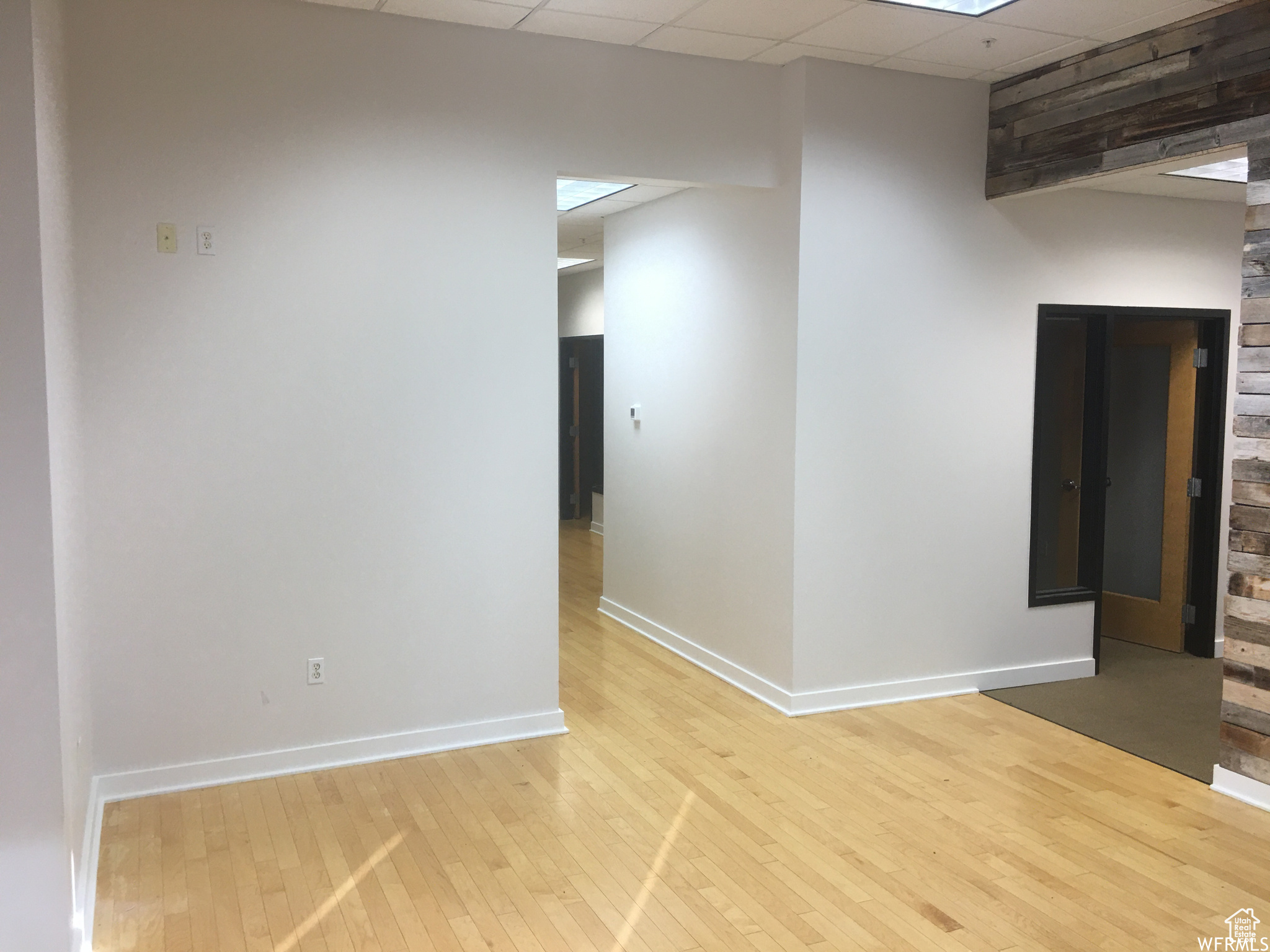 Empty room with a drop ceiling and light hardwood floors