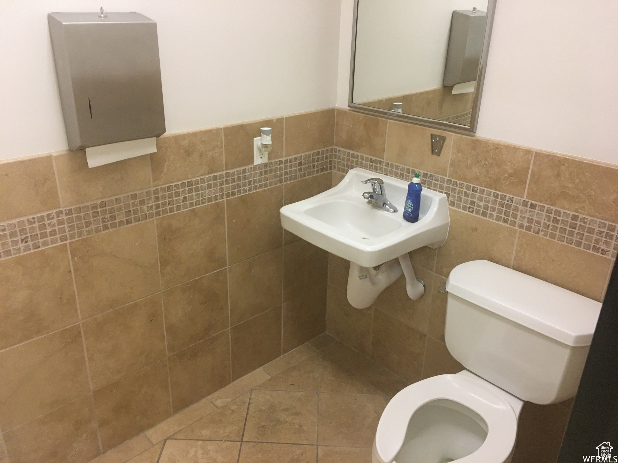 Bathroom featuring mirror, washbasin, backsplash, tile walls, and light tile flooring