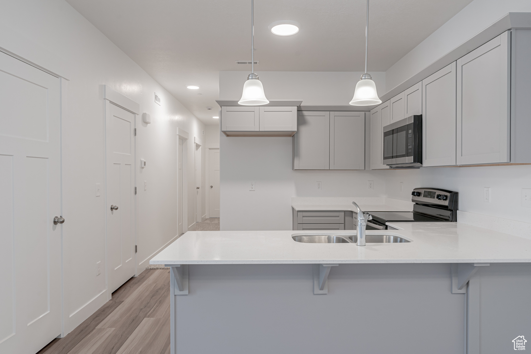 Kitchen featuring light hardwood / wood-style flooring, kitchen peninsula, stainless steel appliances, sink, and pendant lighting