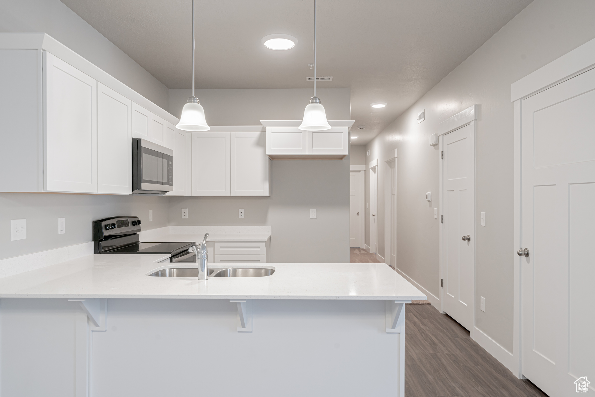 Kitchen with stainless steel appliances, decorative light fixtures, dark wood-type flooring, sink, and white cabinetry