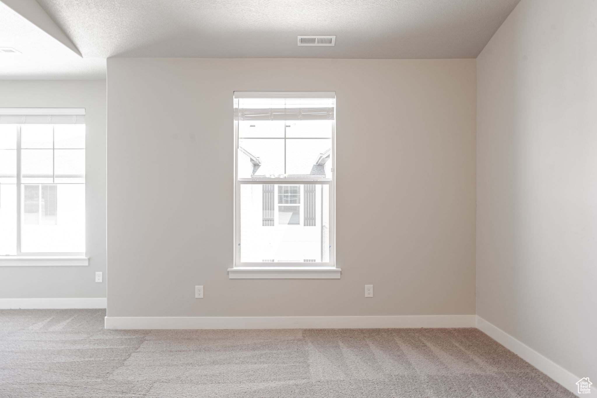 Empty room with light colored carpet and a textured ceiling