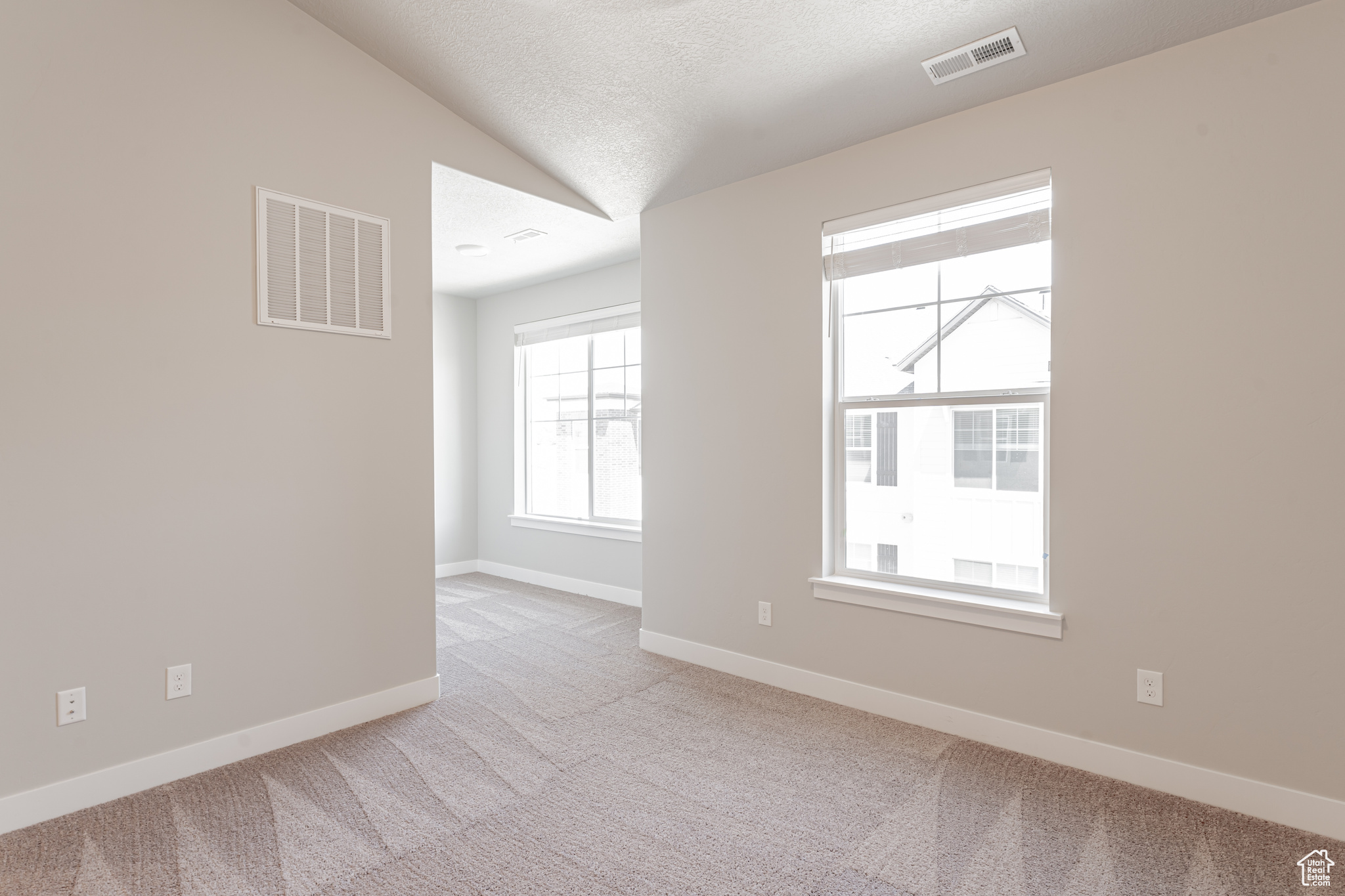 Empty room featuring light carpet, a textured ceiling, and lofted ceiling