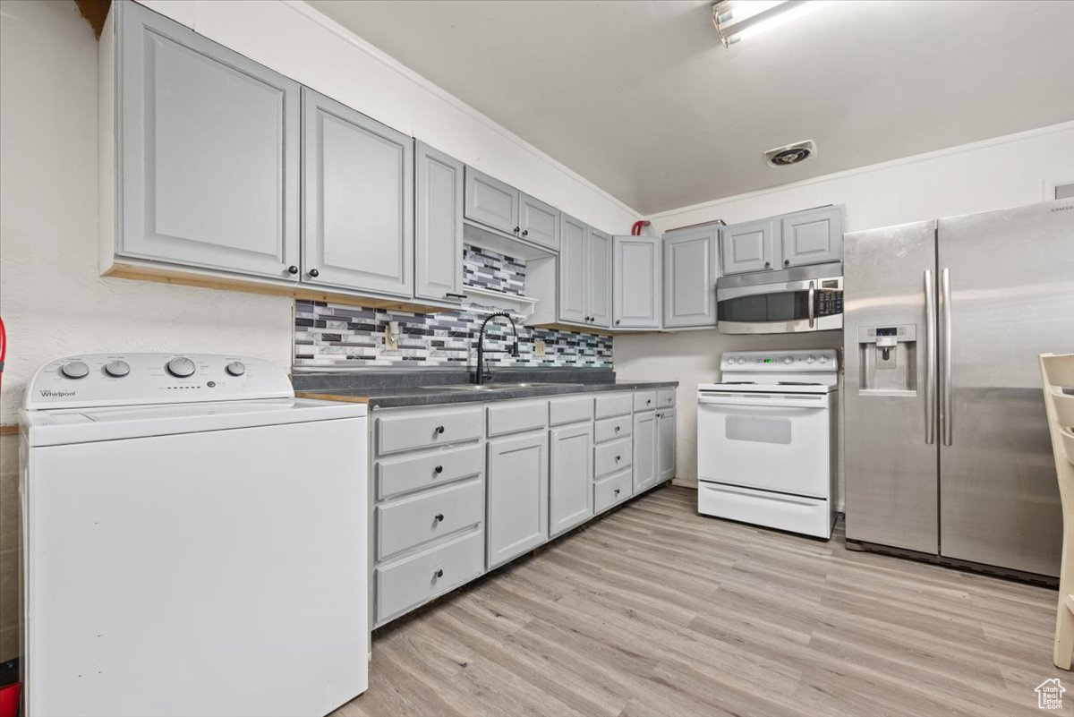Kitchen with appliances with stainless steel finishes, light hardwood / wood-style flooring, sink, washer / dryer, and gray cabinetry
