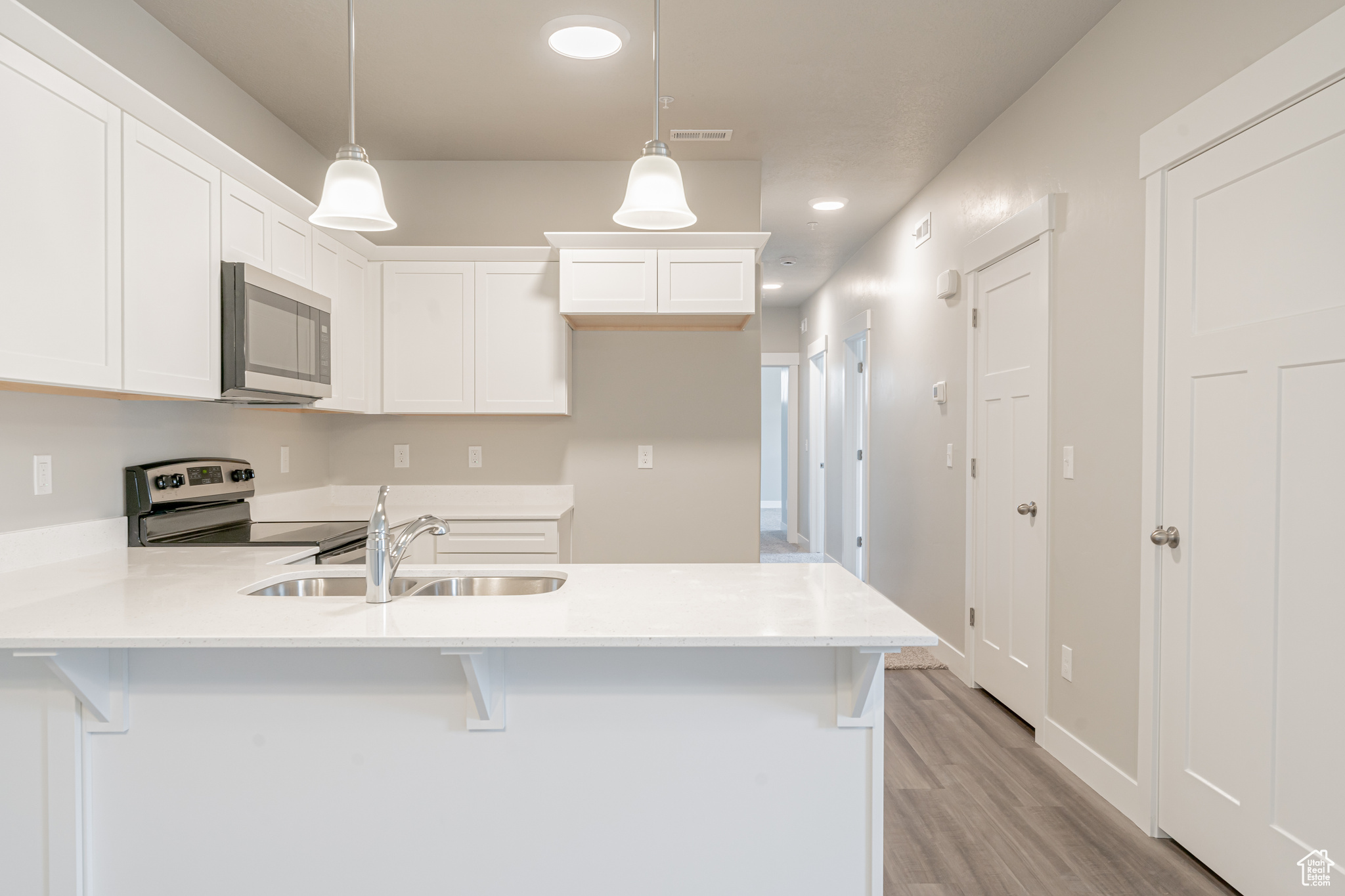 Kitchen with light hardwood / wood-style floors, white cabinetry, stainless steel appliances, and decorative light fixtures