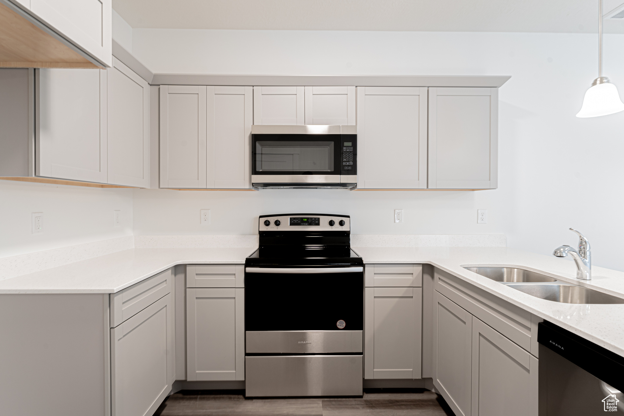 Kitchen with hanging light fixtures, stainless steel appliances, white cabinetry, sink, and wood-type flooring