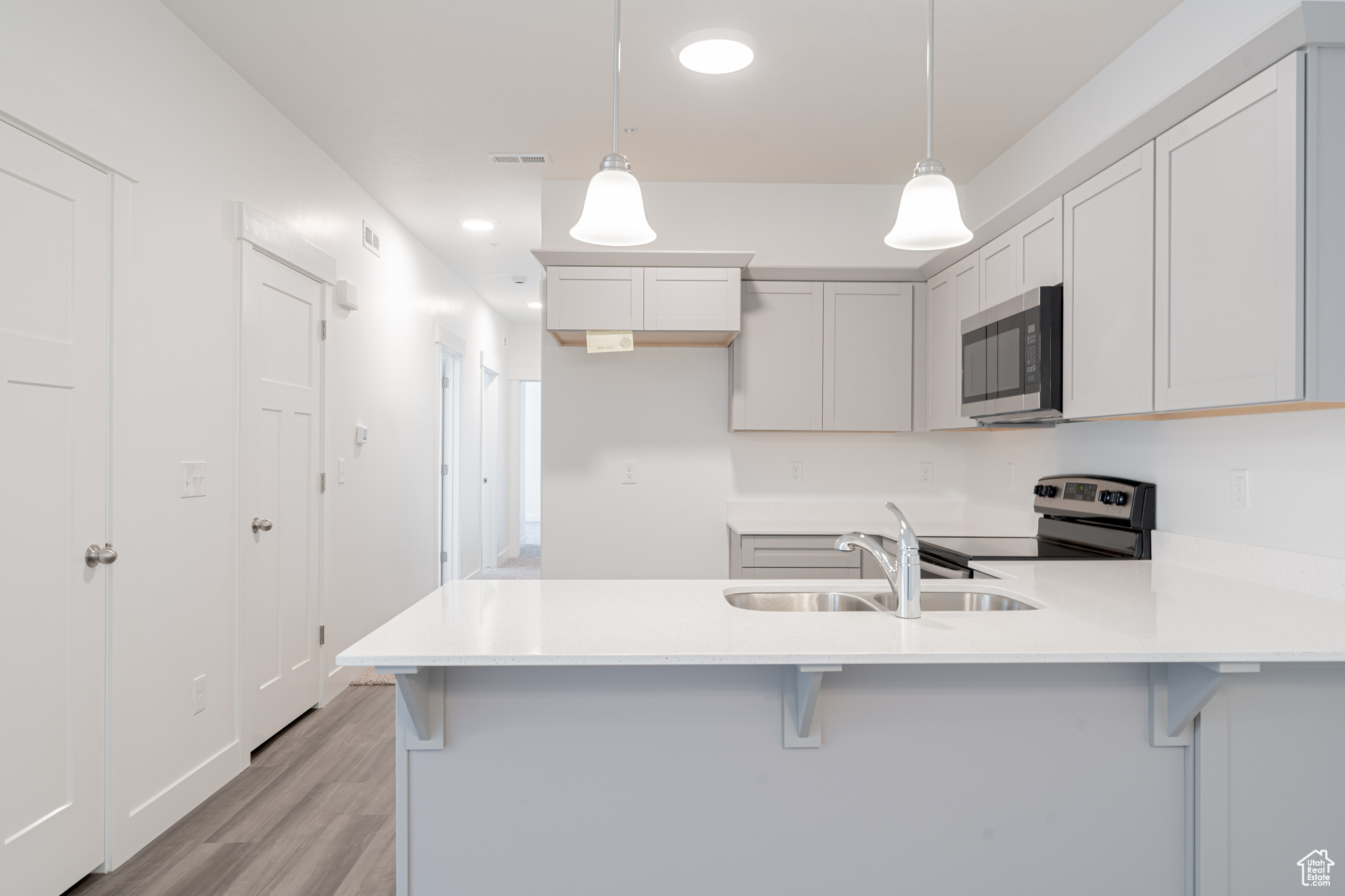 Kitchen featuring pendant lighting, stainless steel appliances, white cabinets, and light hardwood / wood-style floors