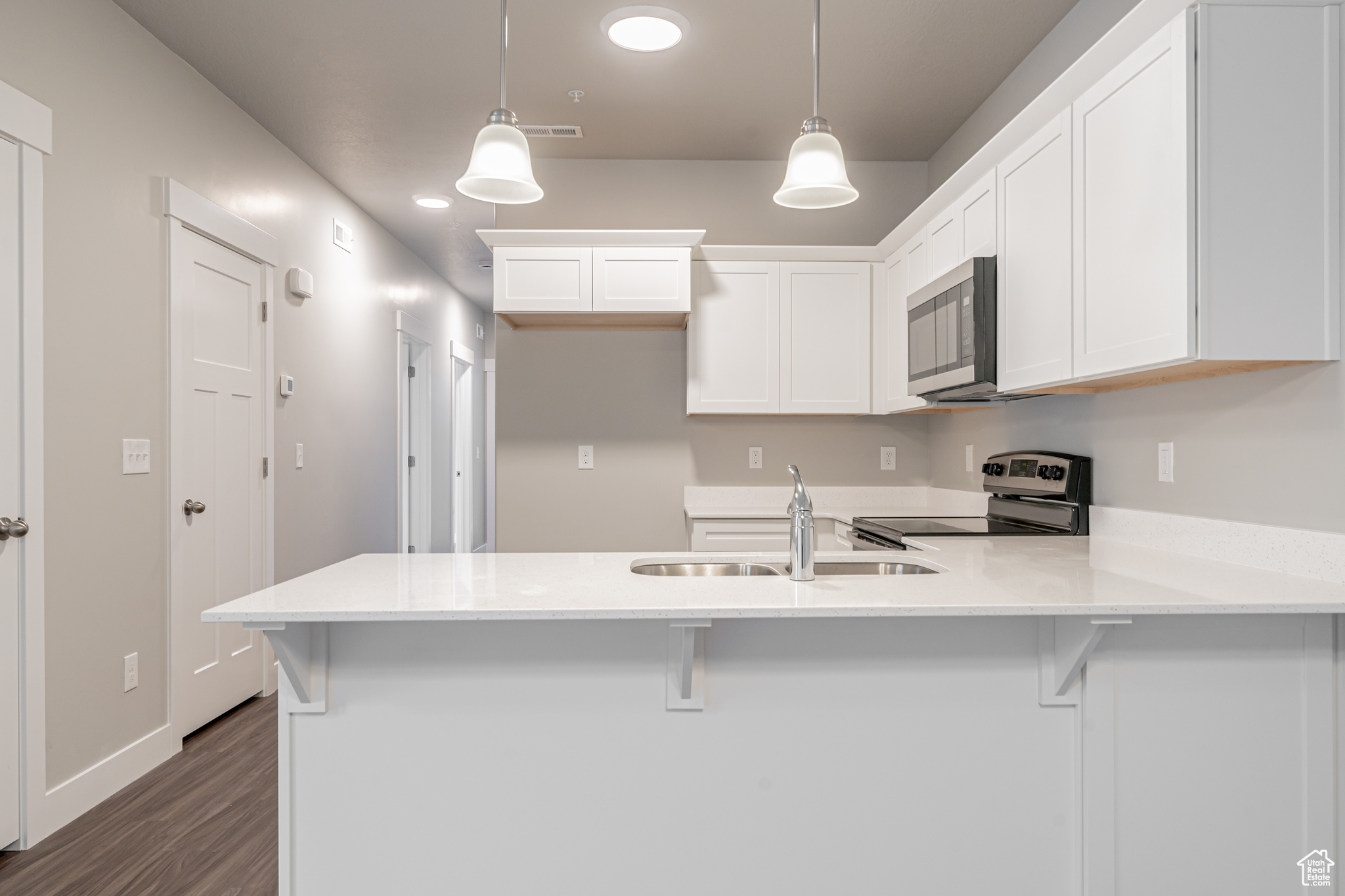 Kitchen featuring hanging light fixtures, white cabinetry, a kitchen bar, dark hardwood / wood-style floors, and appliances with stainless steel finishes