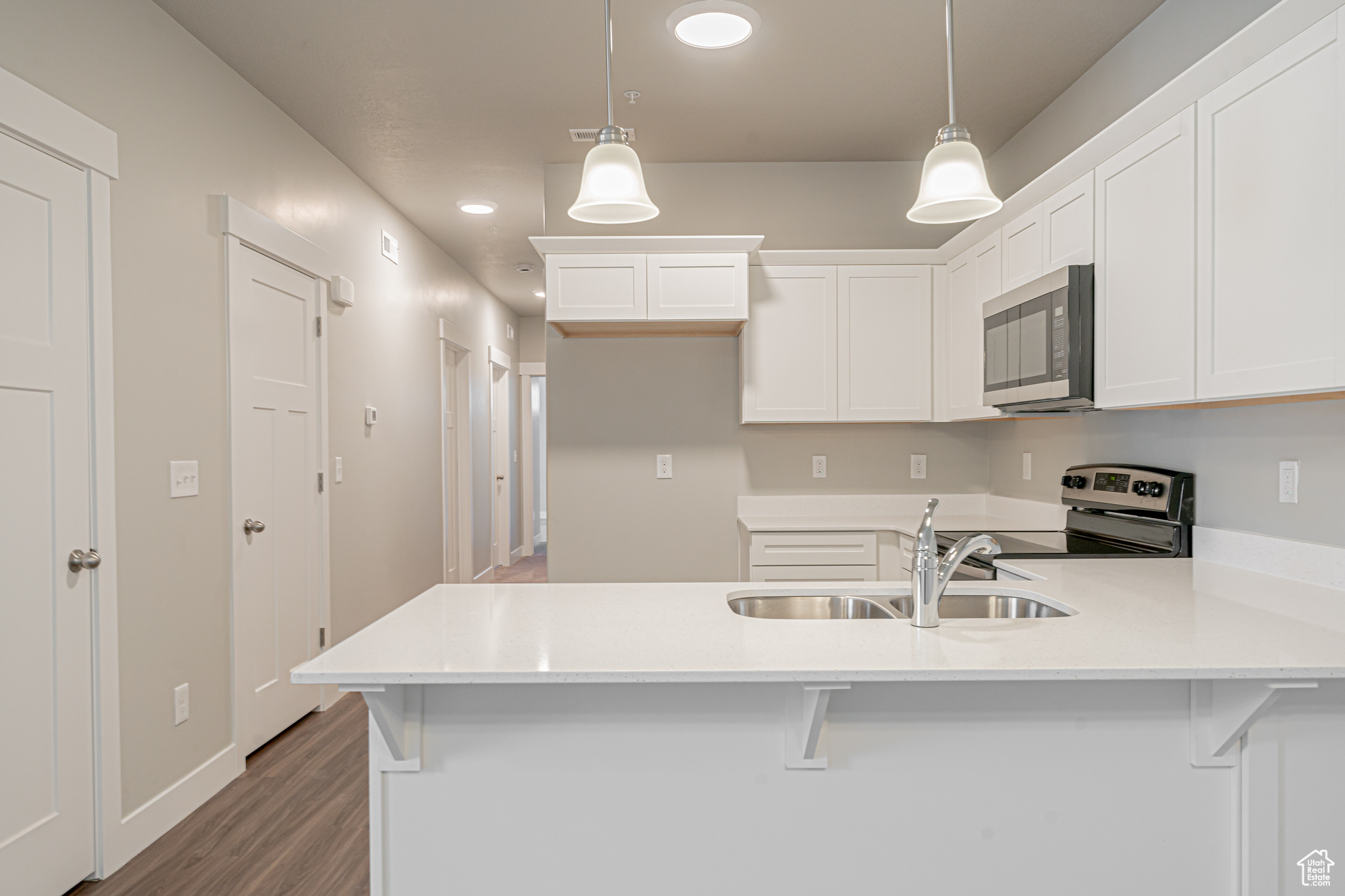 Kitchen with white cabinets, hanging light fixtures, hardwood / wood-style flooring, and electric range oven