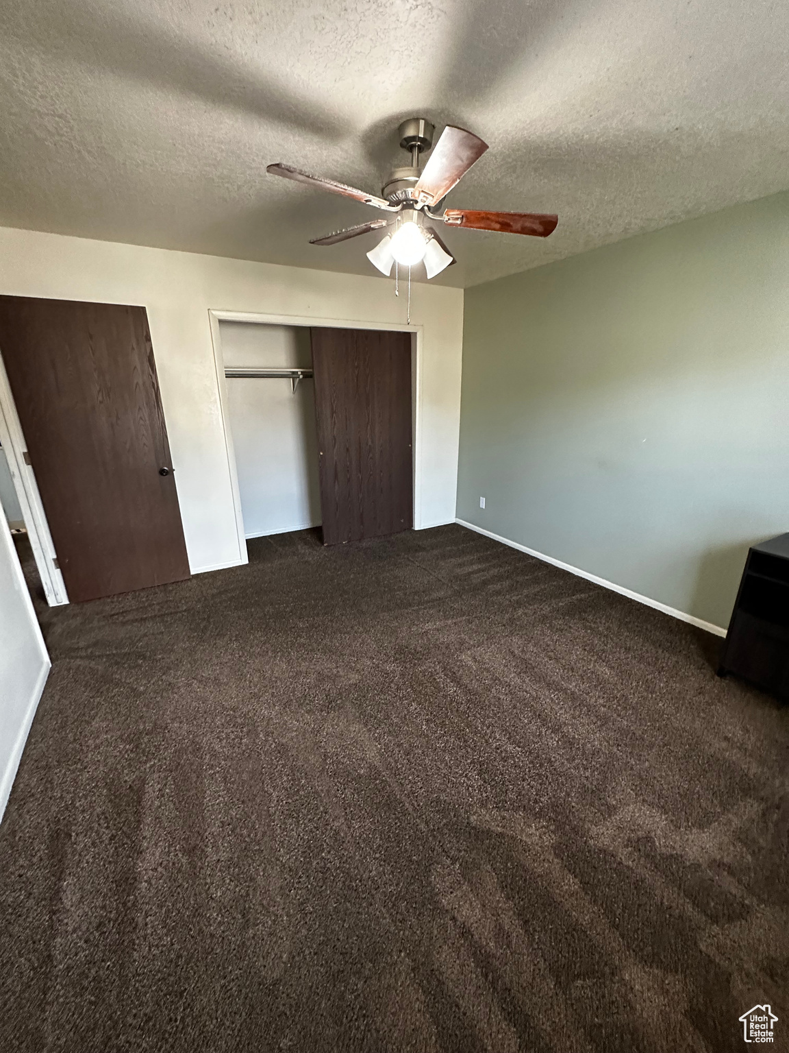 Unfurnished bedroom with a textured ceiling, dark colored carpet, and ceiling fan
