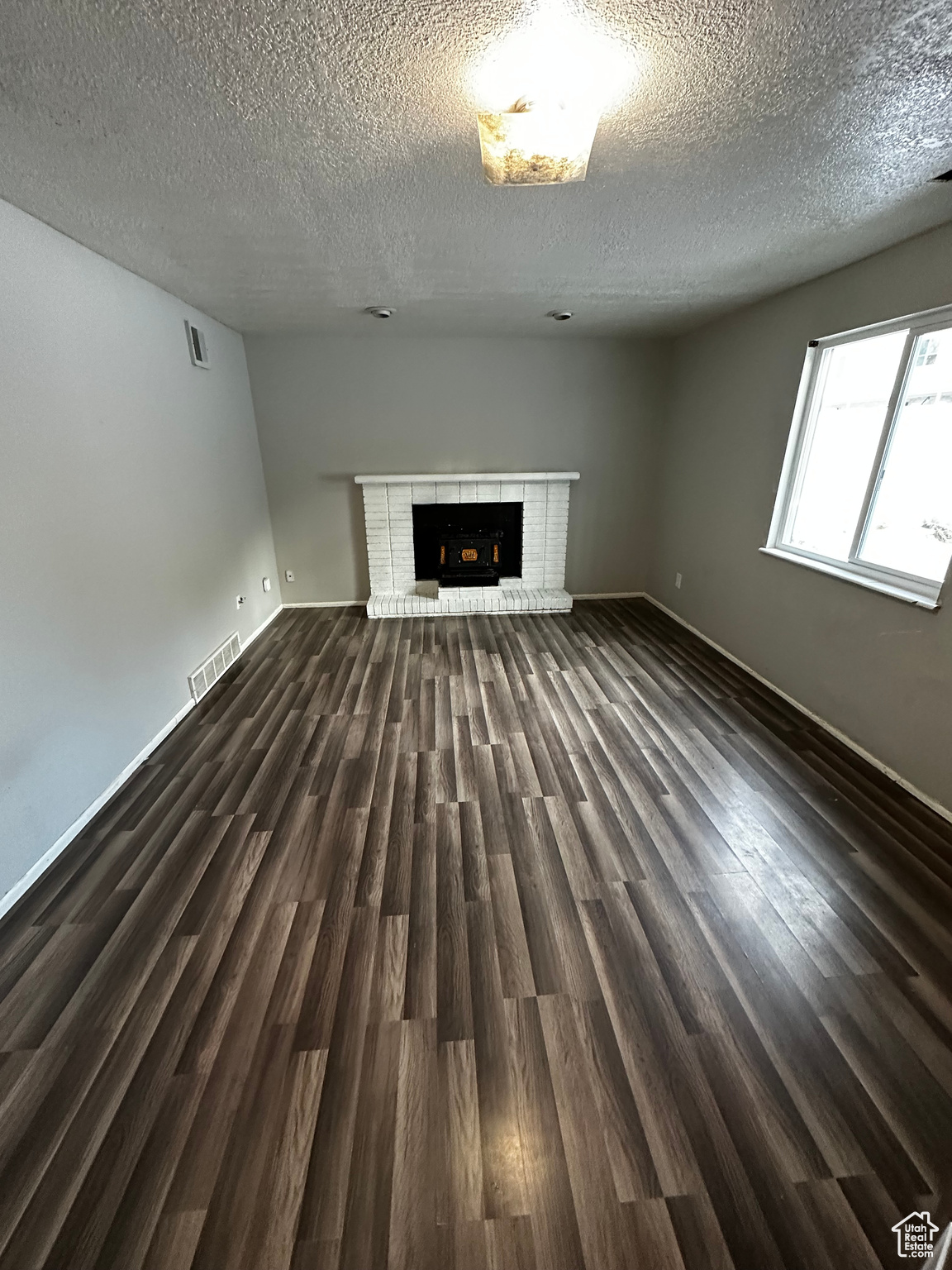 Unfurnished living room with dark hardwood / wood-style flooring, a textured ceiling, and a fireplace
