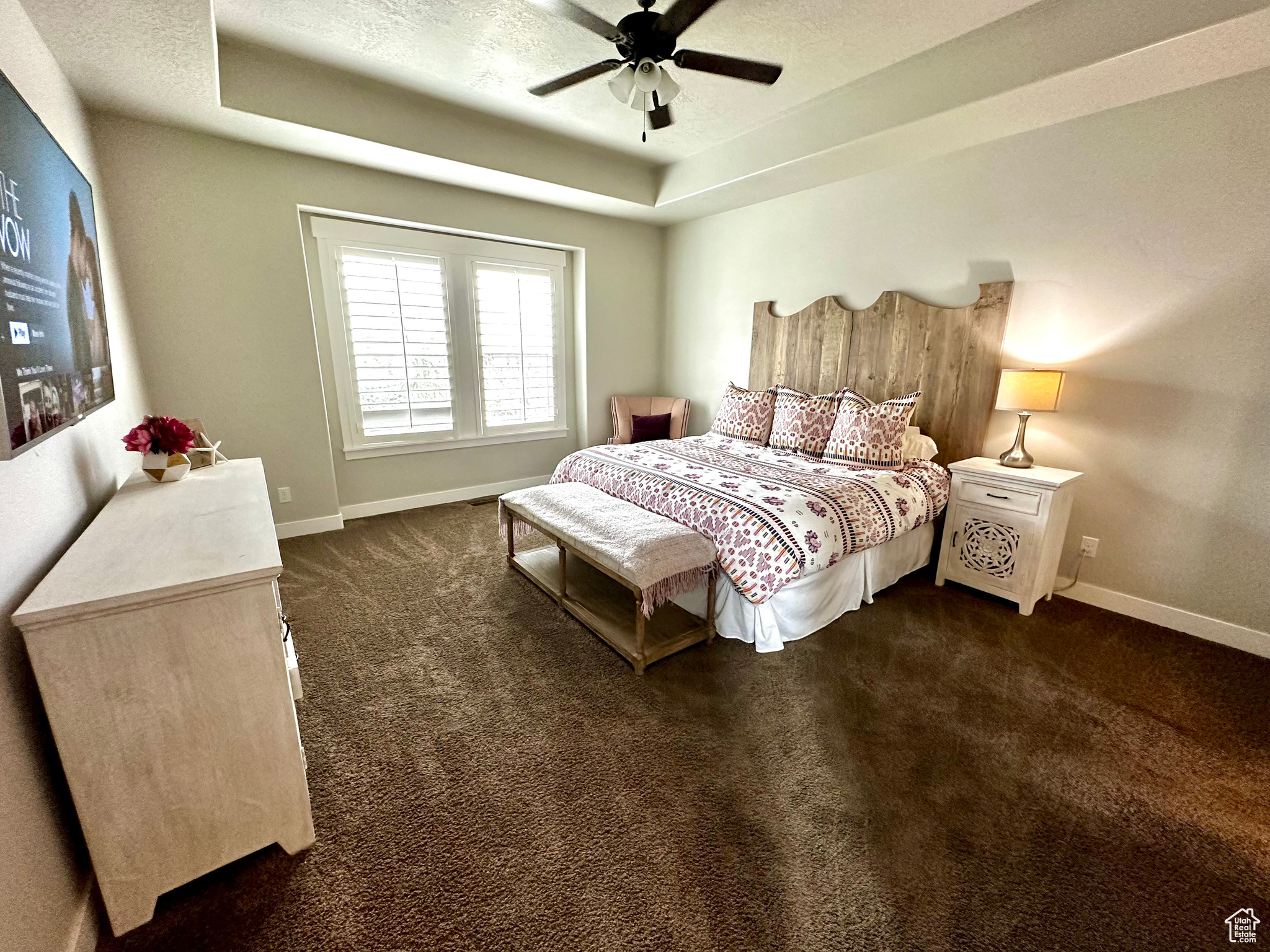 Carpeted bedroom featuring ceiling fan and a raised ceiling