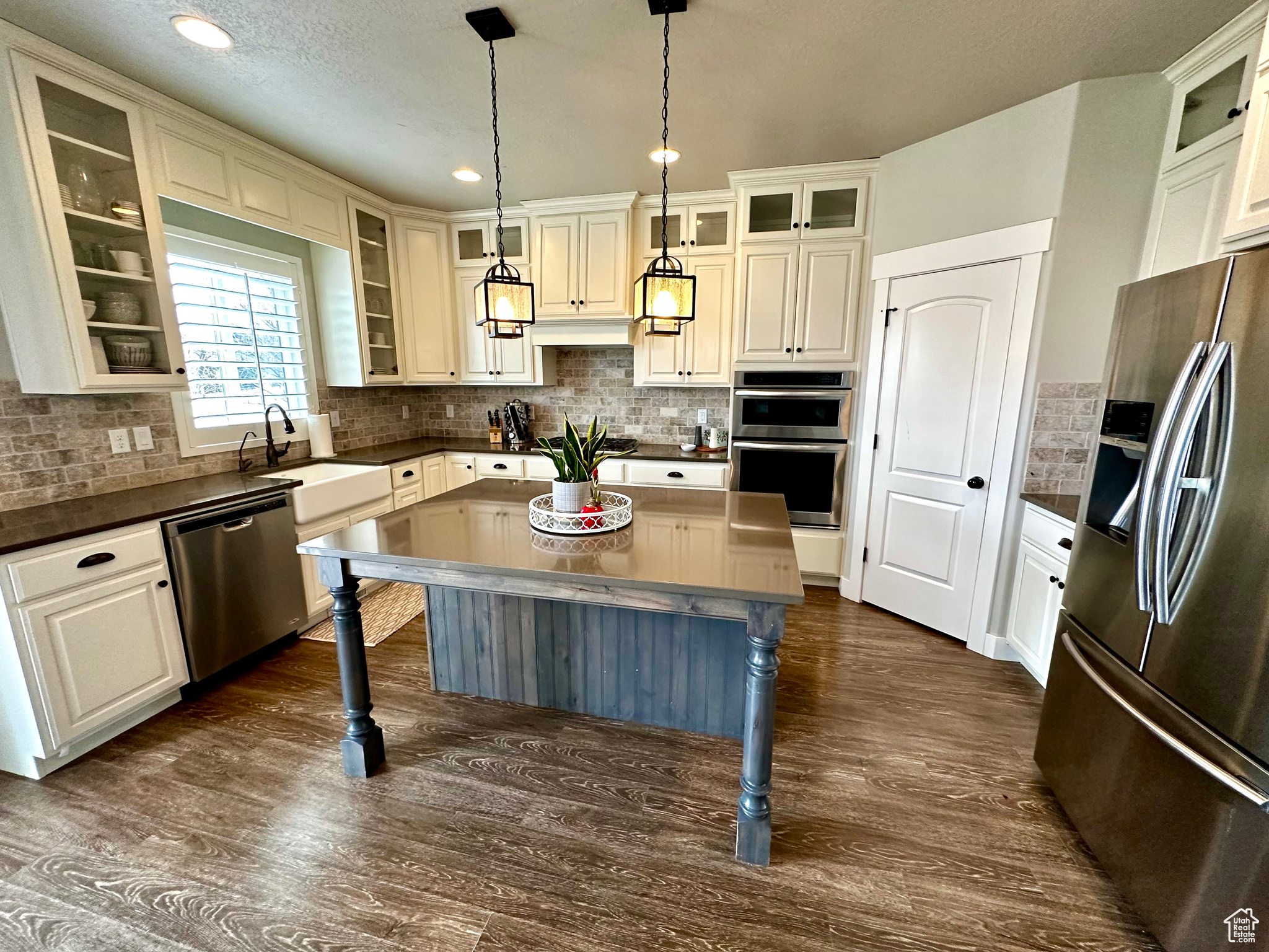 Kitchen featuring dark hardwood / wood-style flooring, stainless steel appliances, backsplash, hanging light fixtures, and a center island