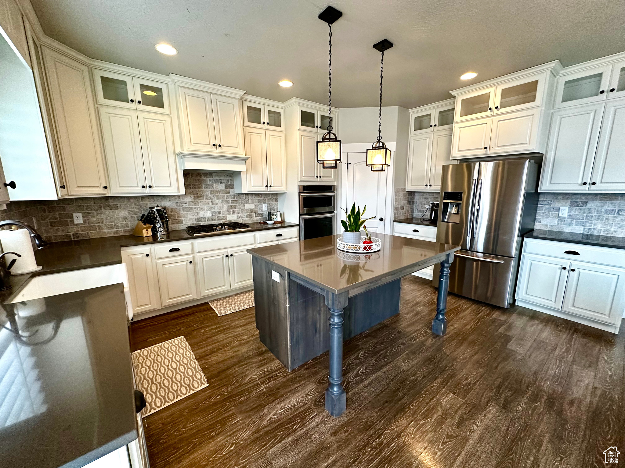 Kitchen with white cabinets, hanging light fixtures, tasteful backsplash, dark hardwood / wood-style flooring, and stainless steel appliances