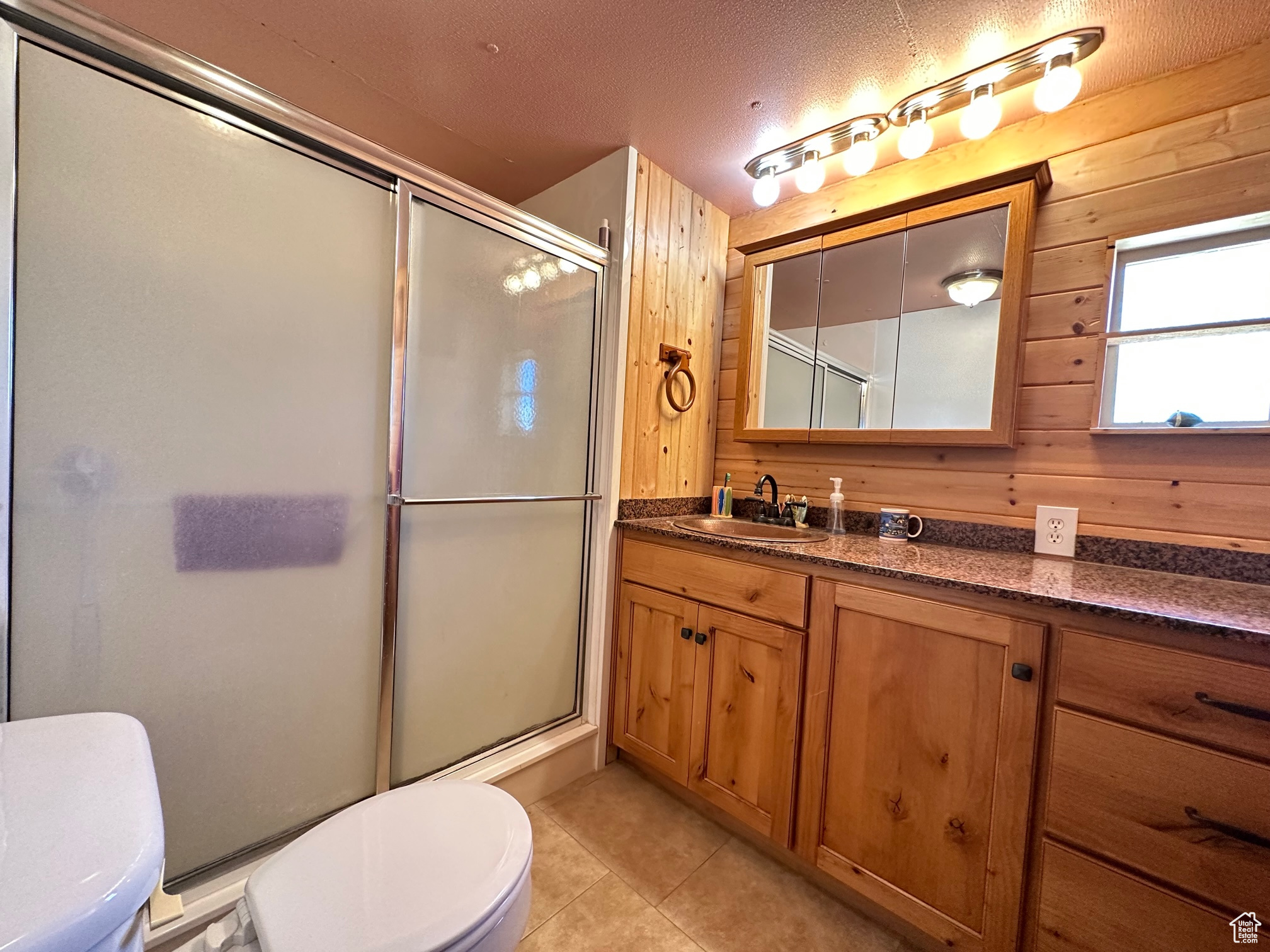 Bathroom with tile floors, wooden walls, vanity, and toilet, tub with shower surround