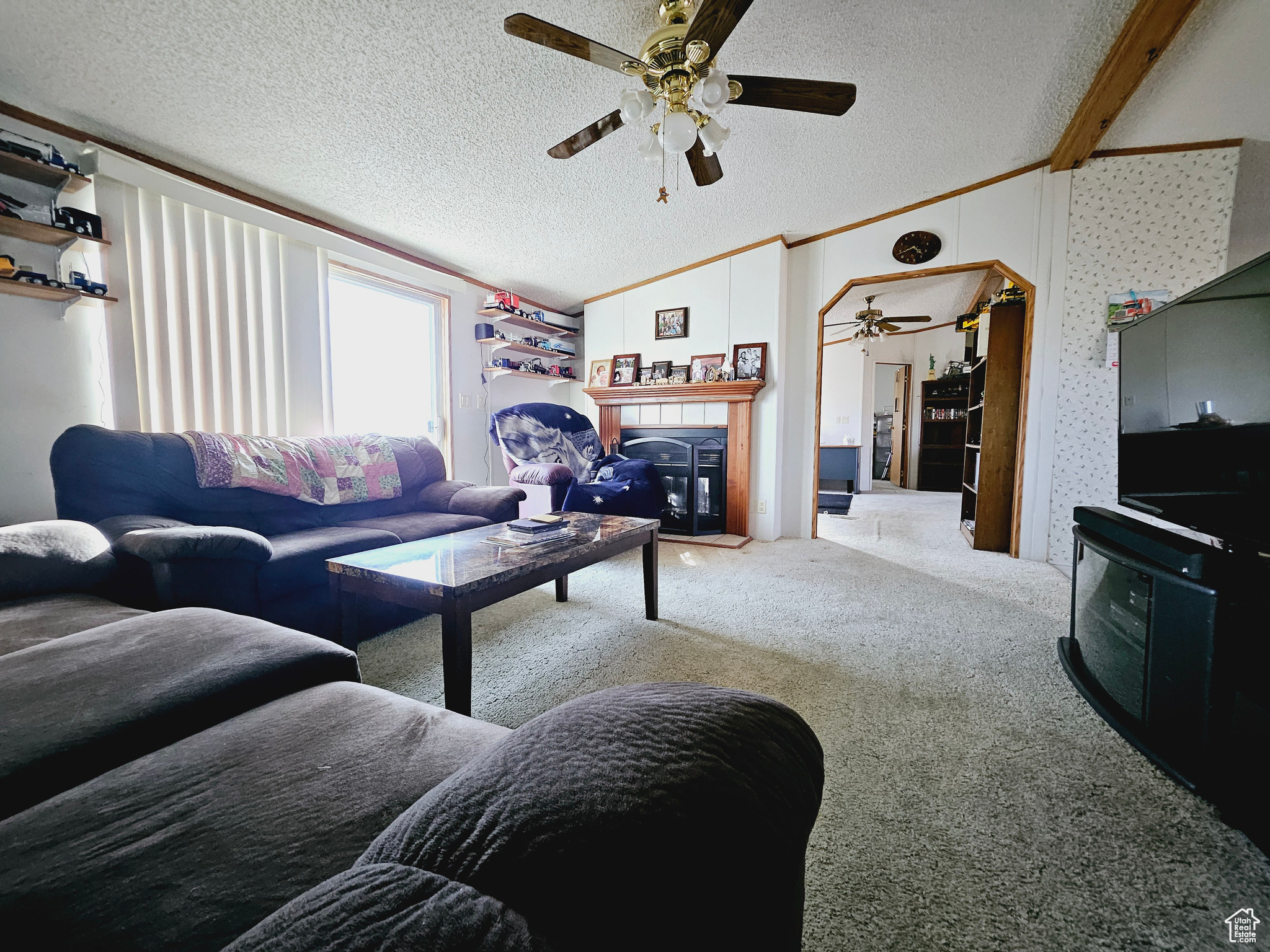 Living room featuring lofted ceiling, light colored carpet, ceiling fan, a textured ceiling, and ornamental molding