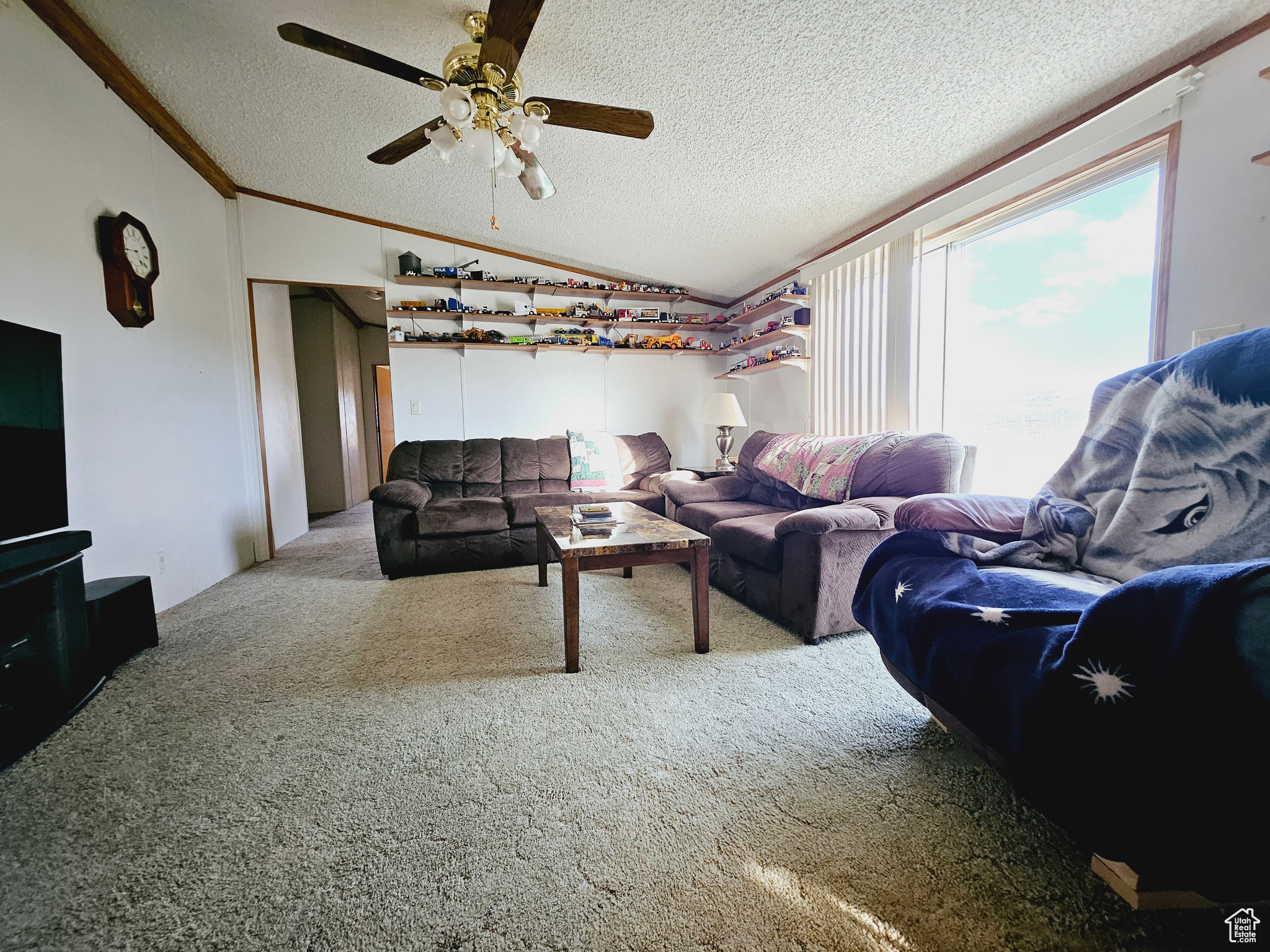 Living room featuring a textured ceiling, vaulted ceiling, ornamental molding, carpet flooring, and ceiling fan