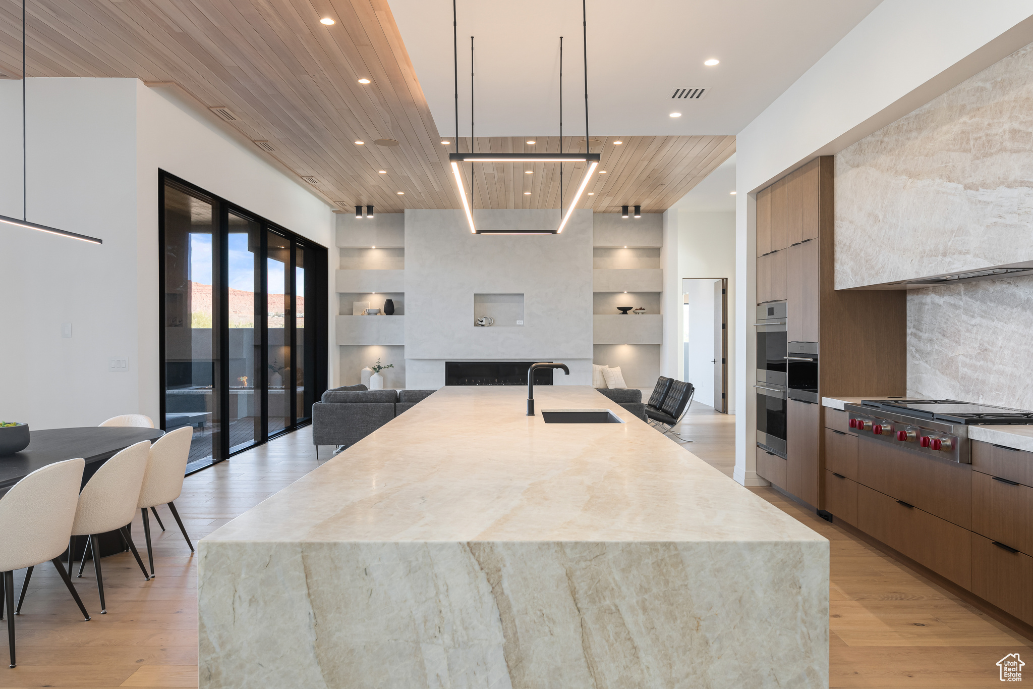 Kitchen with a large island, sink, stainless steel gas cooktop, backsplash, and decorative light fixtures