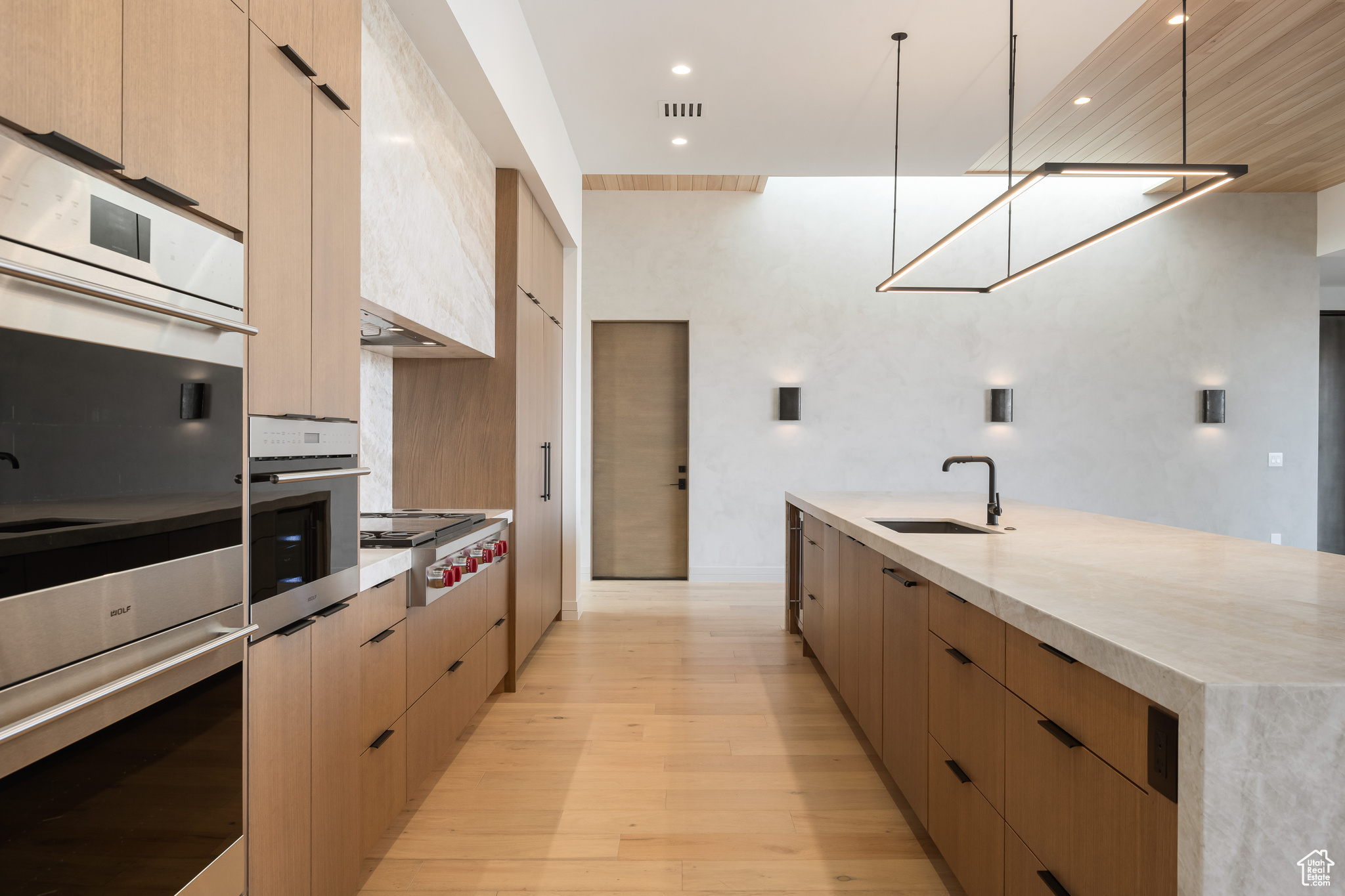 Kitchen with sink, light brown cabinets, hanging light fixtures, light hardwood / wood-style flooring, and appliances with stainless steel finishes