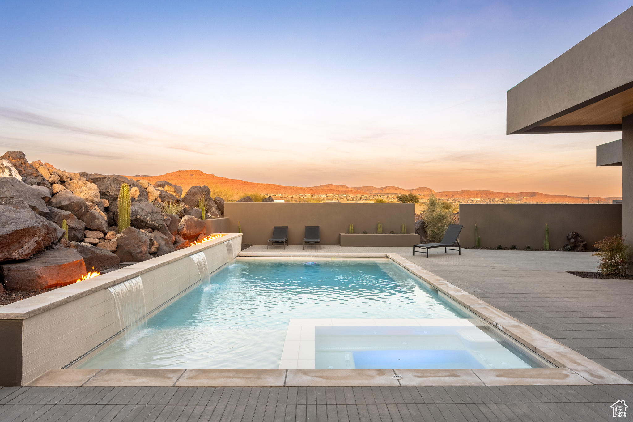 Pool at dusk with a mountain view, an in ground hot tub, pool water feature, and a patio