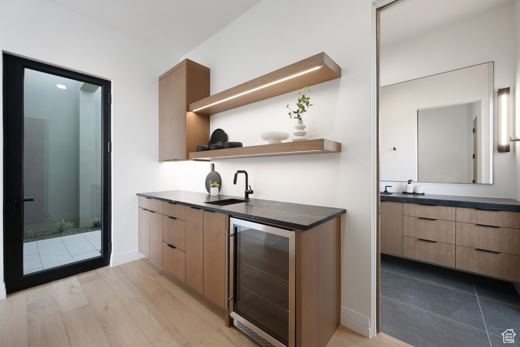 Bar with wine cooler, sink, light brown cabinets, and light wood-type flooring