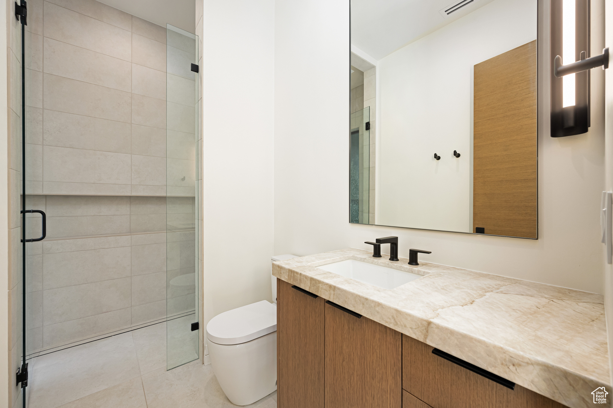 Bathroom featuring tile patterned flooring, vanity, toilet, and a shower with door