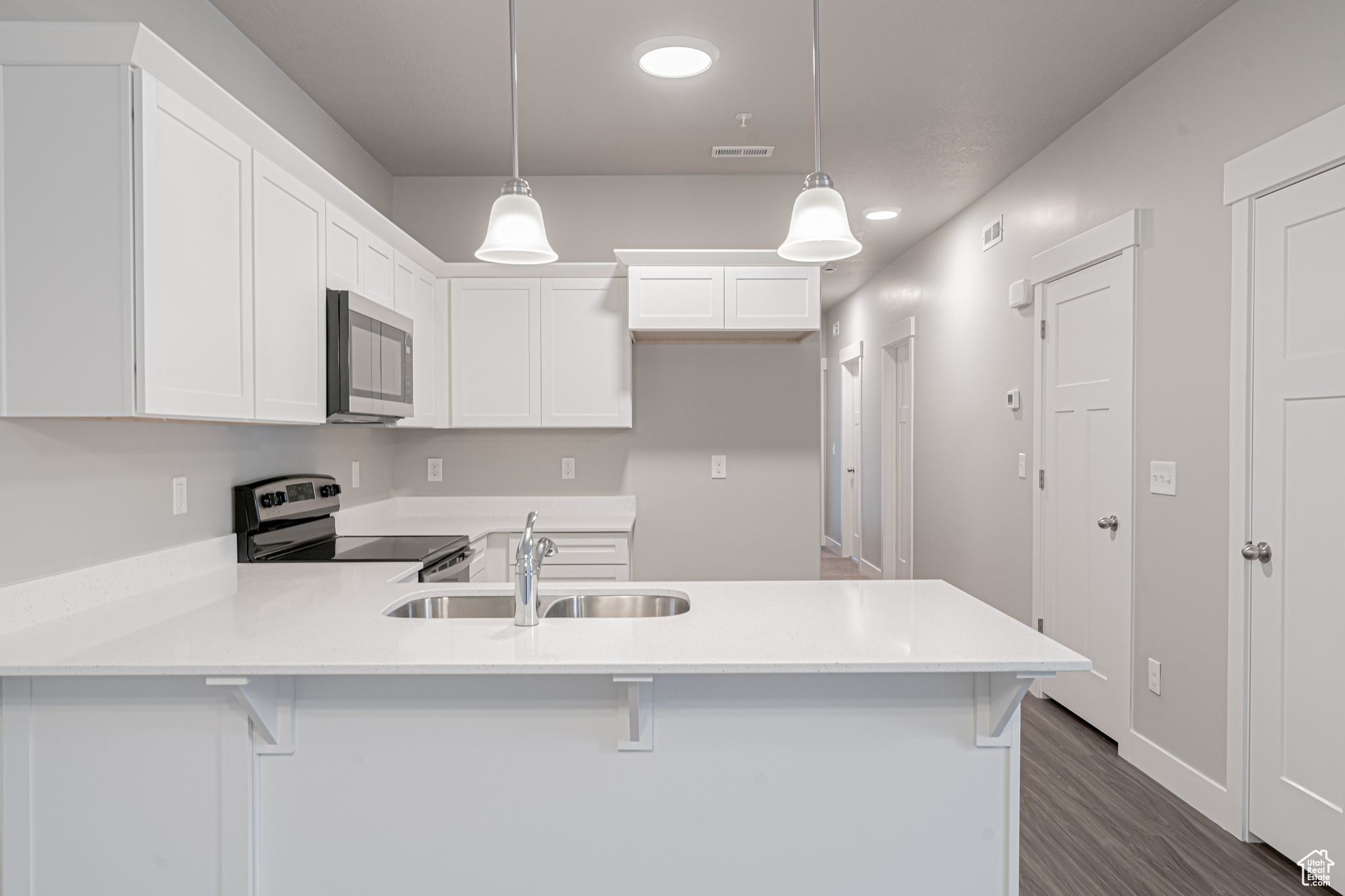 Kitchen featuring white cabinets, dark hardwood / wood-style floors, stainless steel appliances, pendant lighting, and sink