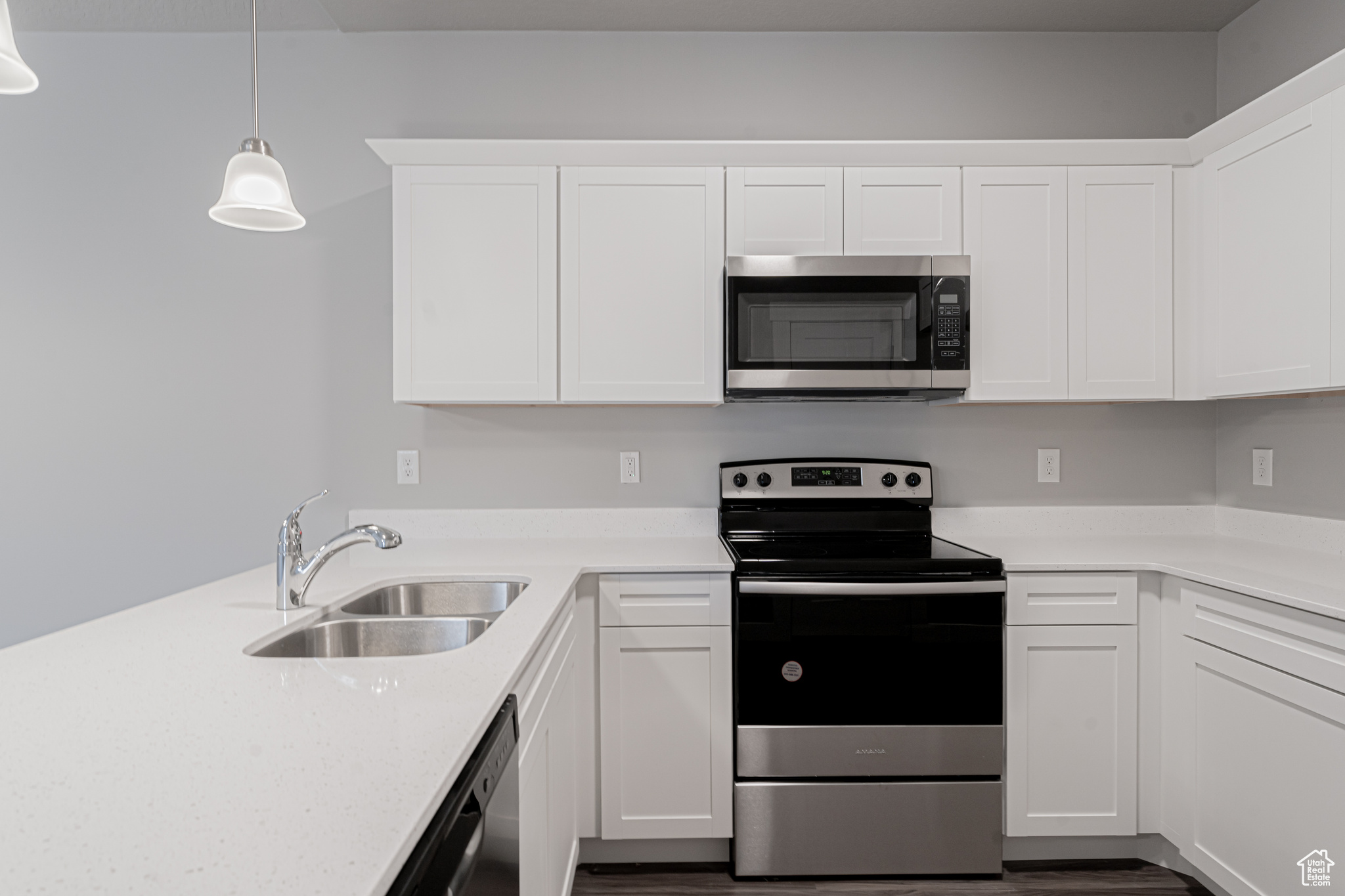 Kitchen with appliances with stainless steel finishes, white cabinets, sink, pendant lighting, and wood-type flooring