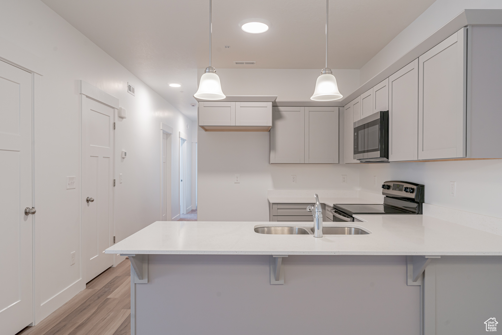 Kitchen with light wood-type flooring, kitchen peninsula, stainless steel appliances, decorative light fixtures, and sink