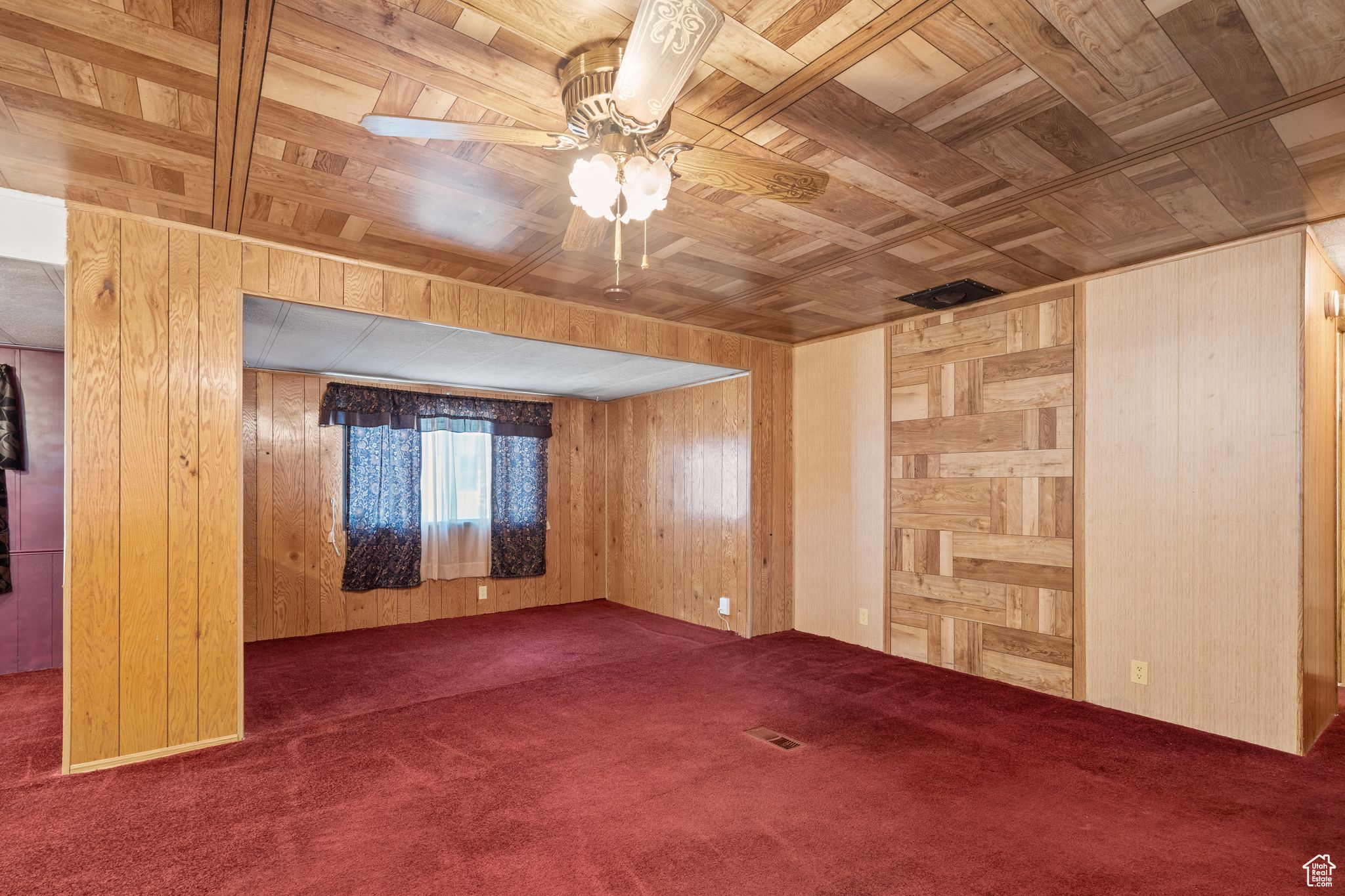 Empty room featuring wooden ceiling, dark colored carpet, wood walls, and ceiling fan