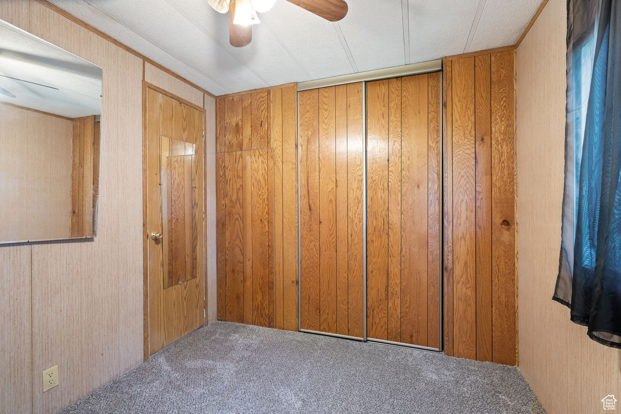 Carpeted spare room featuring wooden walls and ceiling fan