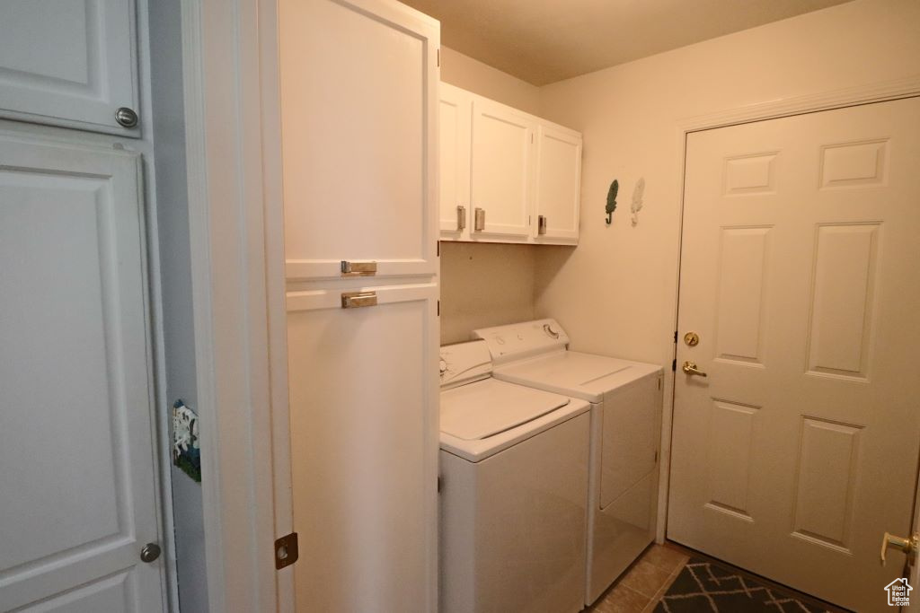 Washroom with dark tile floors, cabinets, and washing machine and clothes dryer