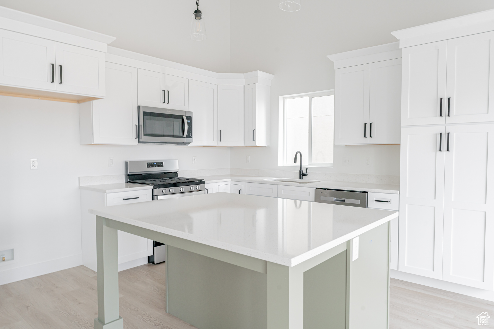 Kitchen with light hardwood / wood-style flooring, a kitchen island, sink, white cabinets, and appliances with stainless steel finishes